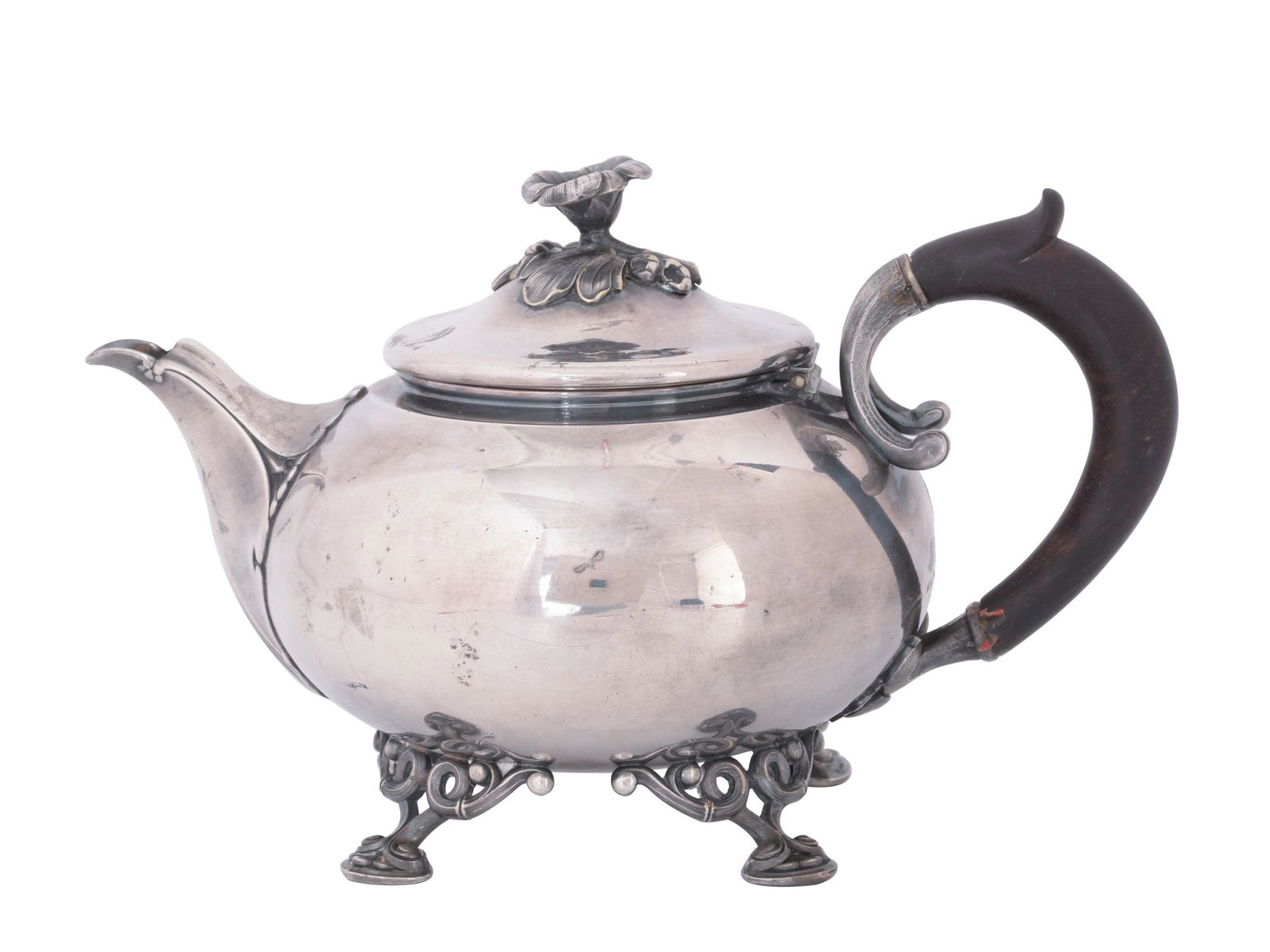 Christofle Silverplate Teapot, 19th Century: A silverplate teapot by Christofle and dating from the 19th century. It stands on four ornate feet, and it has a leaf-form spout. The hinged lid features a floral finial, and the pot has a carved wood