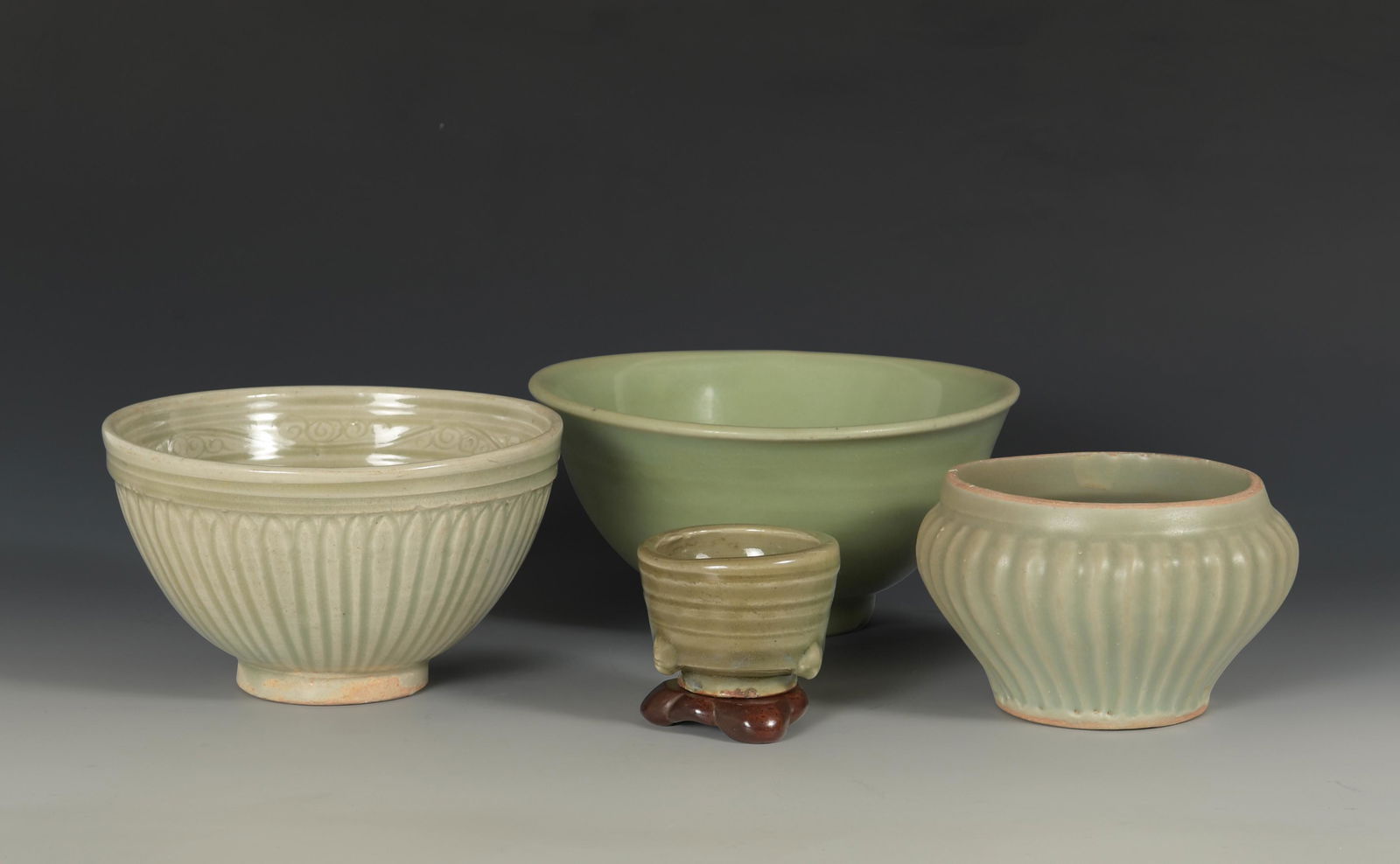 Group of 4 Longquan Porcelains, Song or Yuan: A group of 4 Chinese longquan celadon porcelains dating from the Song or Yuan dynasties. The group includes: a small censer with a wood stand, ribbed bowl, lotus bowl, and bowl with an incised flower