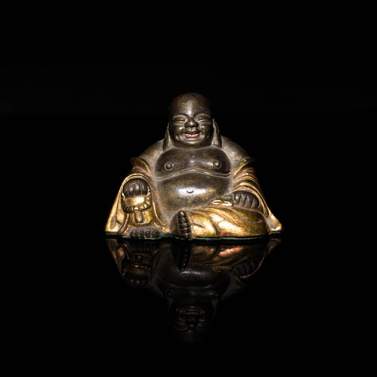 A Chinese gilt-bronze Budai, 18th to the 19th century: A Chinese gilt-bronze Budai 18th to the 19th century Seated grinning Budai figure with gilt robe and red with white painted mouth. Felt-lined underside. H: 2 3/8, W: 3 1/2, D: 2 3/8 in. (H: 6.03, W: 8