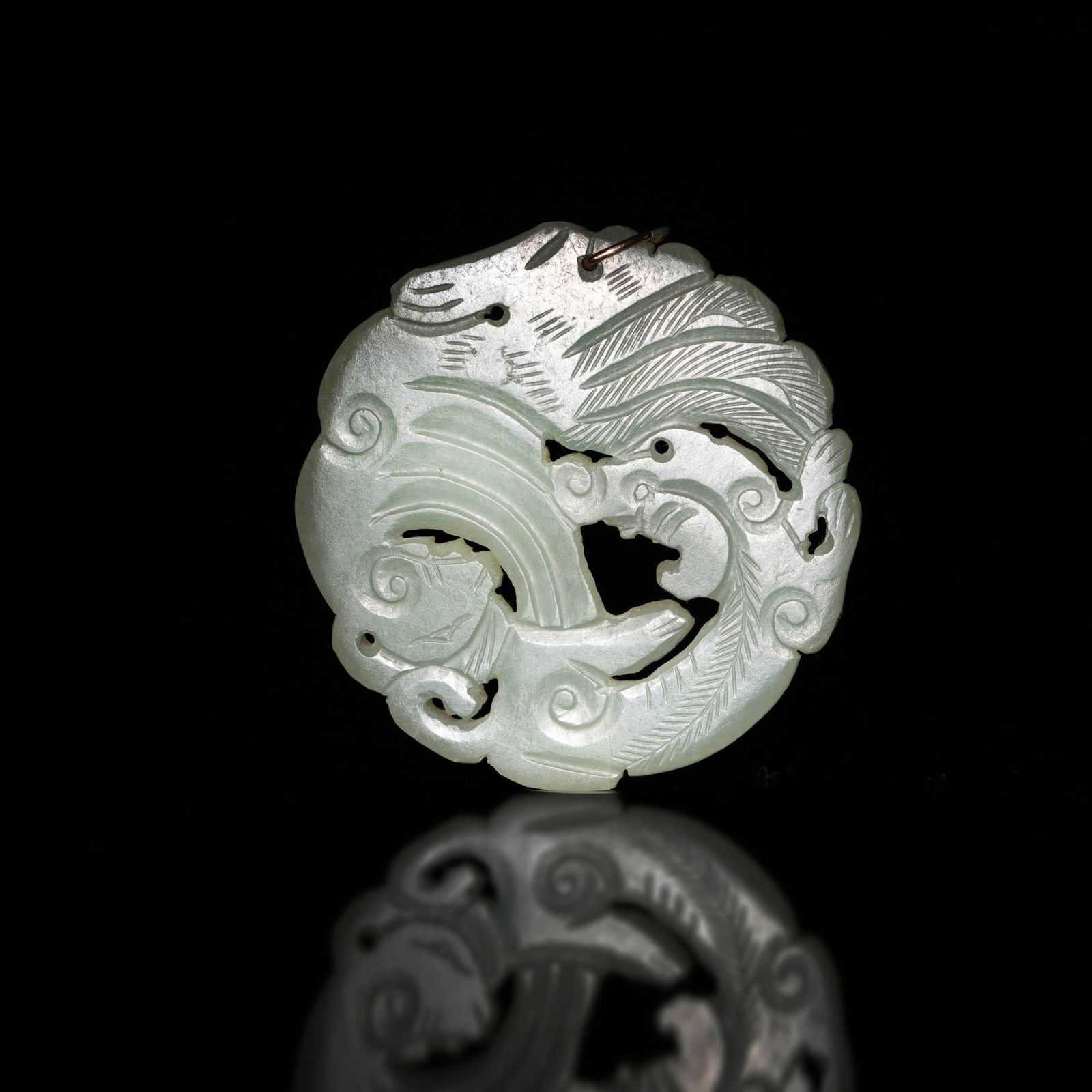 A Chinese celadon jade circular plaque, 18th/19th century: A Chinese celadon jade circular plaque 18th/19th century Featuring a phoenix and a dragon design. Drill hole to circle edge, with jewelry loop. Dia: 2 1/4, D: 1/4 in. Dia: 5.72, D: 0.63 cm. Provenance