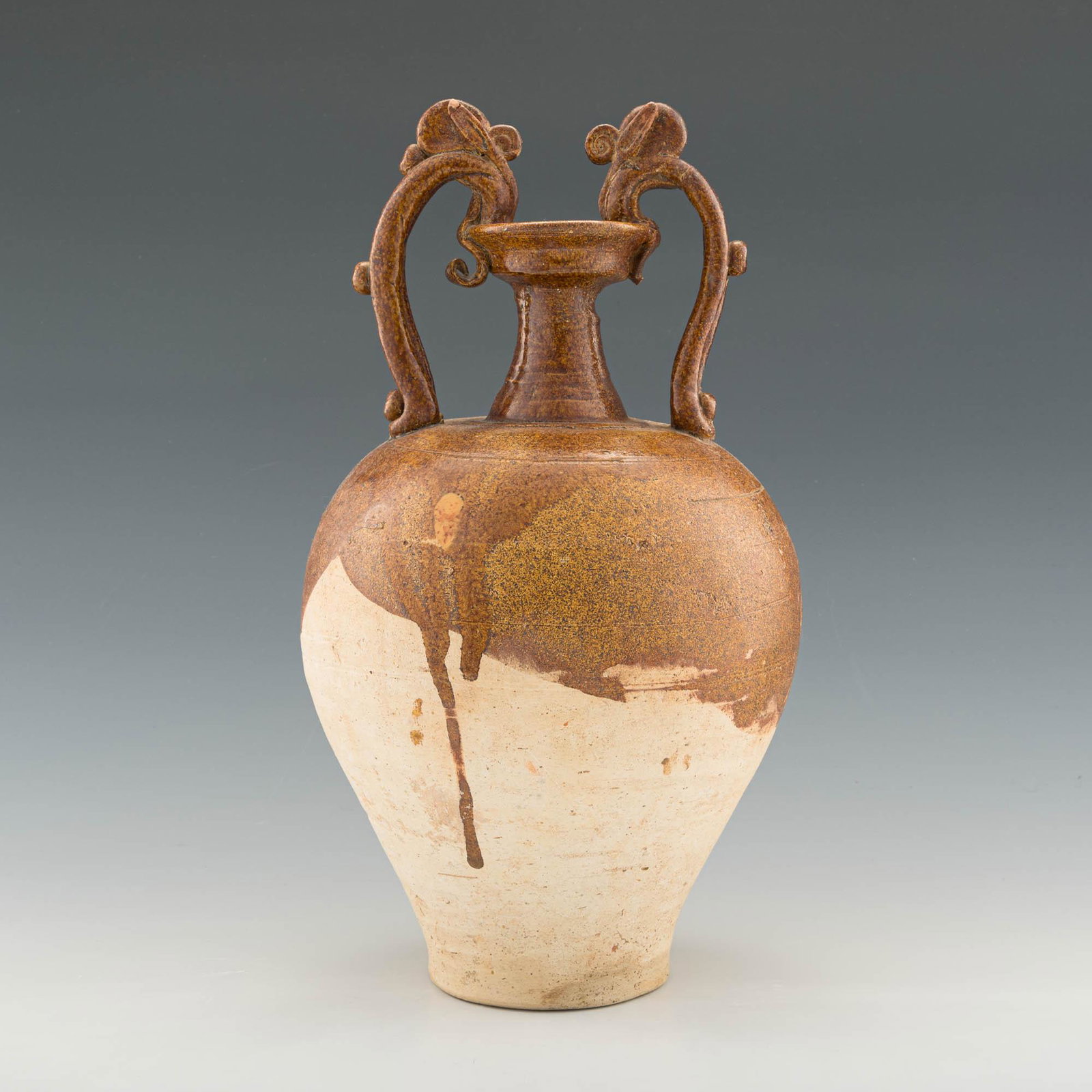 A Chinese brown-glazed amphora, Tang dynasty: A Chinese brown-glazed amphora Tang dynasty A globular vessel tapering to the foot with a pair of dragon-form handles rising from the rounded shoulders and biting the rim. Brown glaze to the upper hal