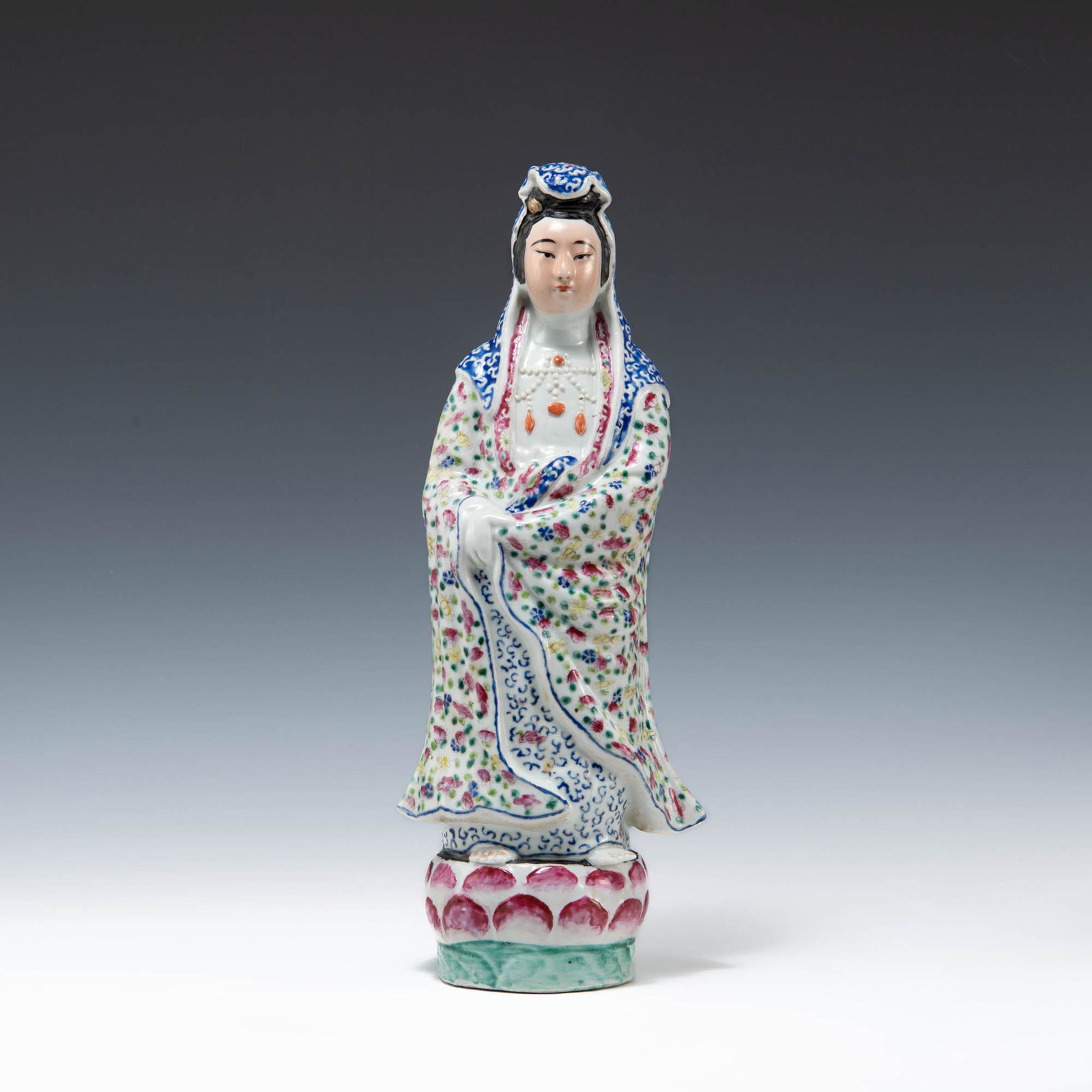 A Chinese famille rose figure of Guanyin, Republic period: A Chinese famille rose figure of Guanyin Republic period A standing figure of Guanyin, clothed in a white robe with flowers and green leaves, and a blue and white head scarf and stands atop a lotus ba