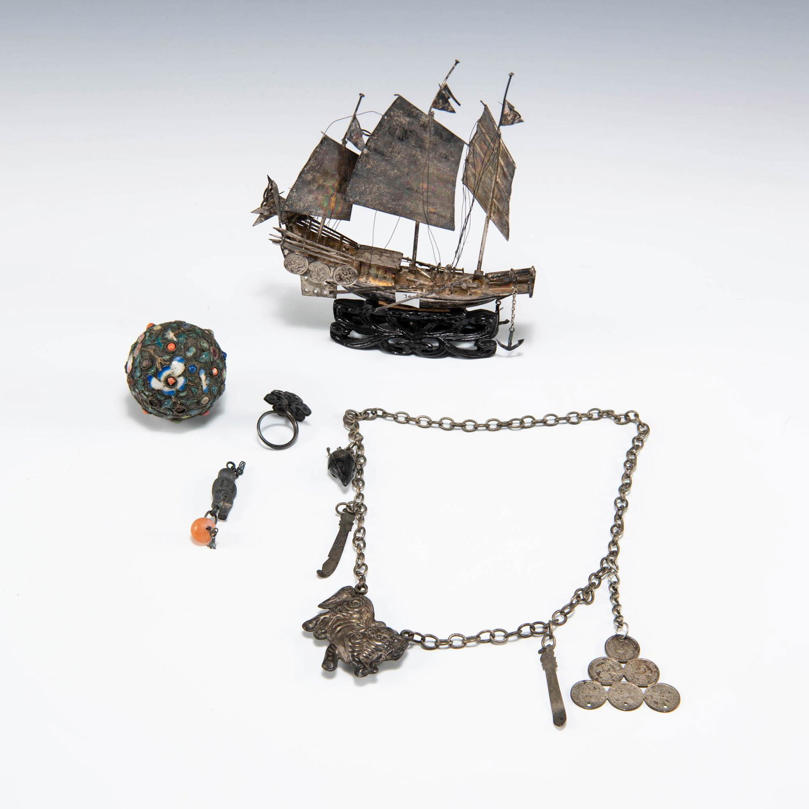 A group of four Chinese metal and silver items, late 19th century: A group of four Chinese metal and silver items late 19th century Comprising a ship model; a flower-form ring with Shou character to center; an enameled ball with flower motifs; a necklace with five me