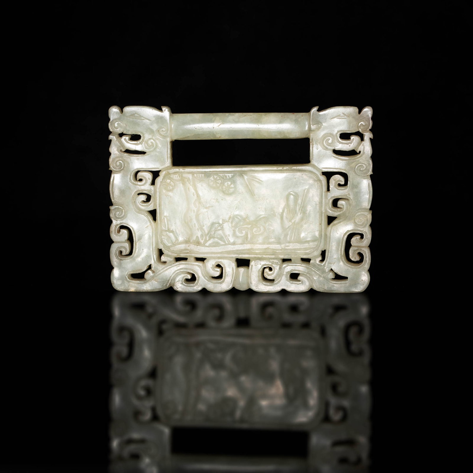 A Chinese carved jade lock-form plaque, 18th century or earlier: A Chinese carved jade lock-form plaque 18th century or earlier One side with four-character inscription, reverse with figural scene, framed on either side by a stylized dragon. H: 2 5/8, W: 3 5/8, D: 