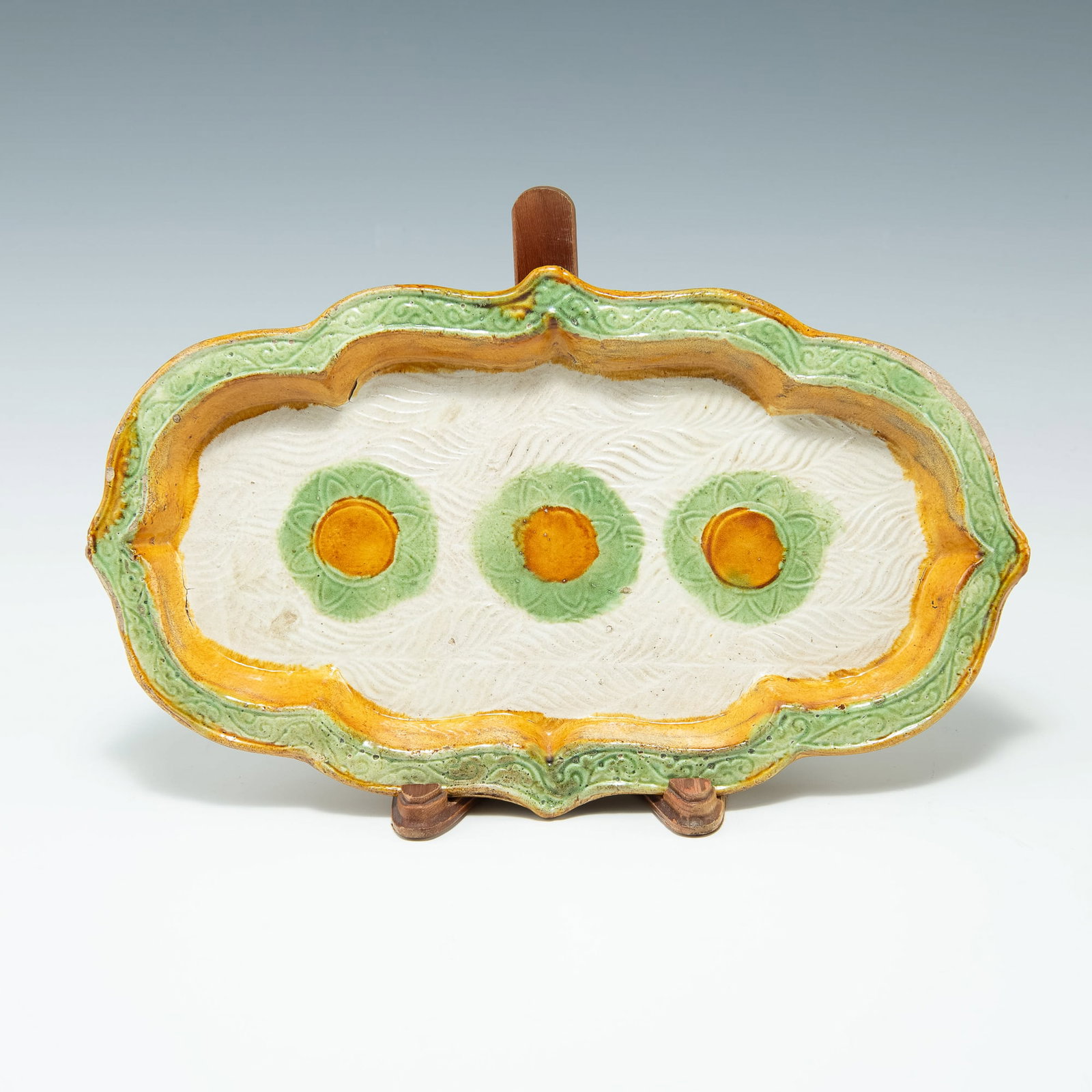 A Chinese sancai-glazed lobed plate, Tang dynasty: A Chinese sancai-glazed lobed plate Tang dynasty The white-ground interior centering three green and yellow flowers with previous collectorâ€™s mark to underside. Sold with associated wooden disp