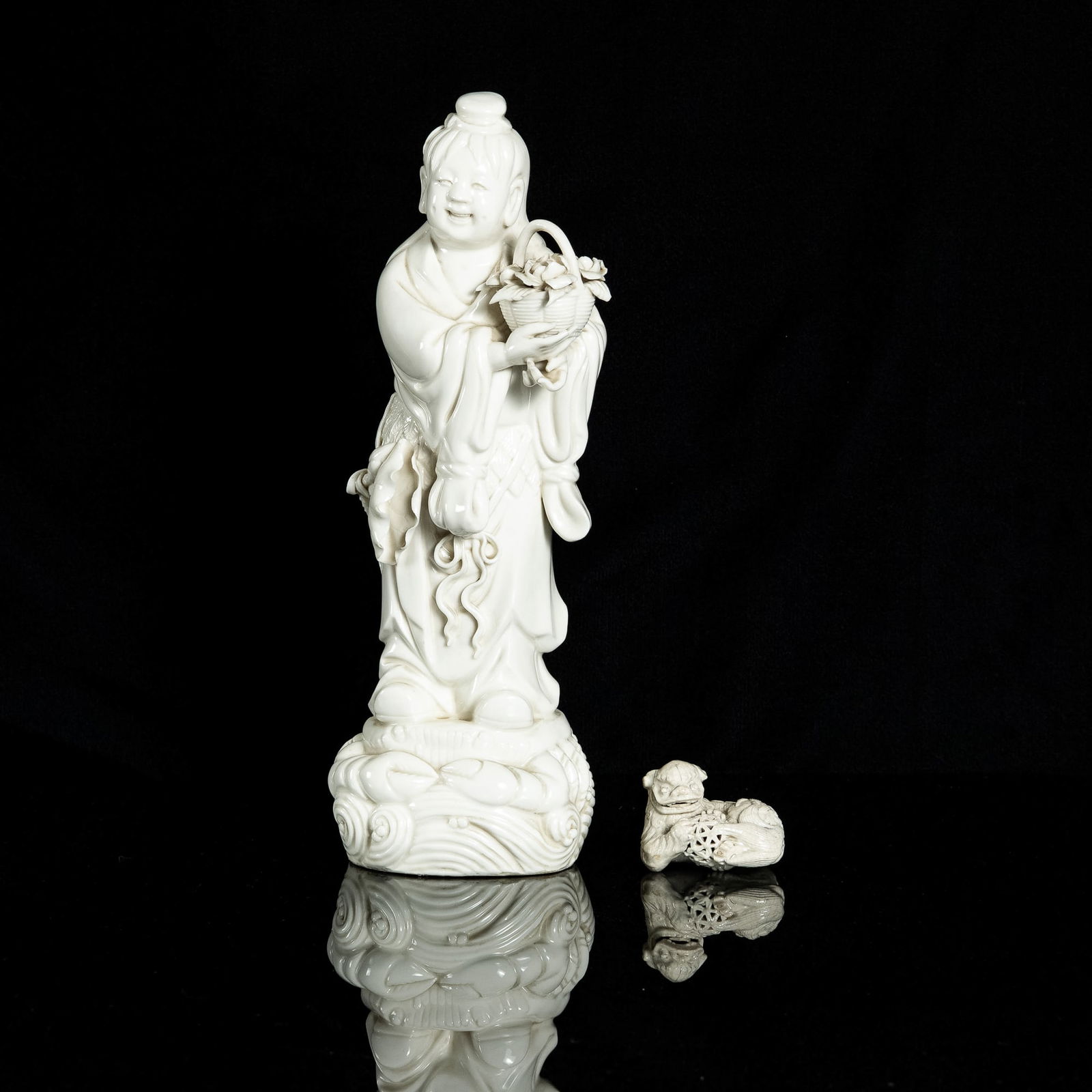 Two Chinese blanc-de-chine figures of boy and lion, 19th century: Two Chinese blanc-de-chine figures of boy and lion 19th century Comprising one small figure of a lion with intricately carved fur pattern holding a ball; and a statue of a robed boy holding a basket o
