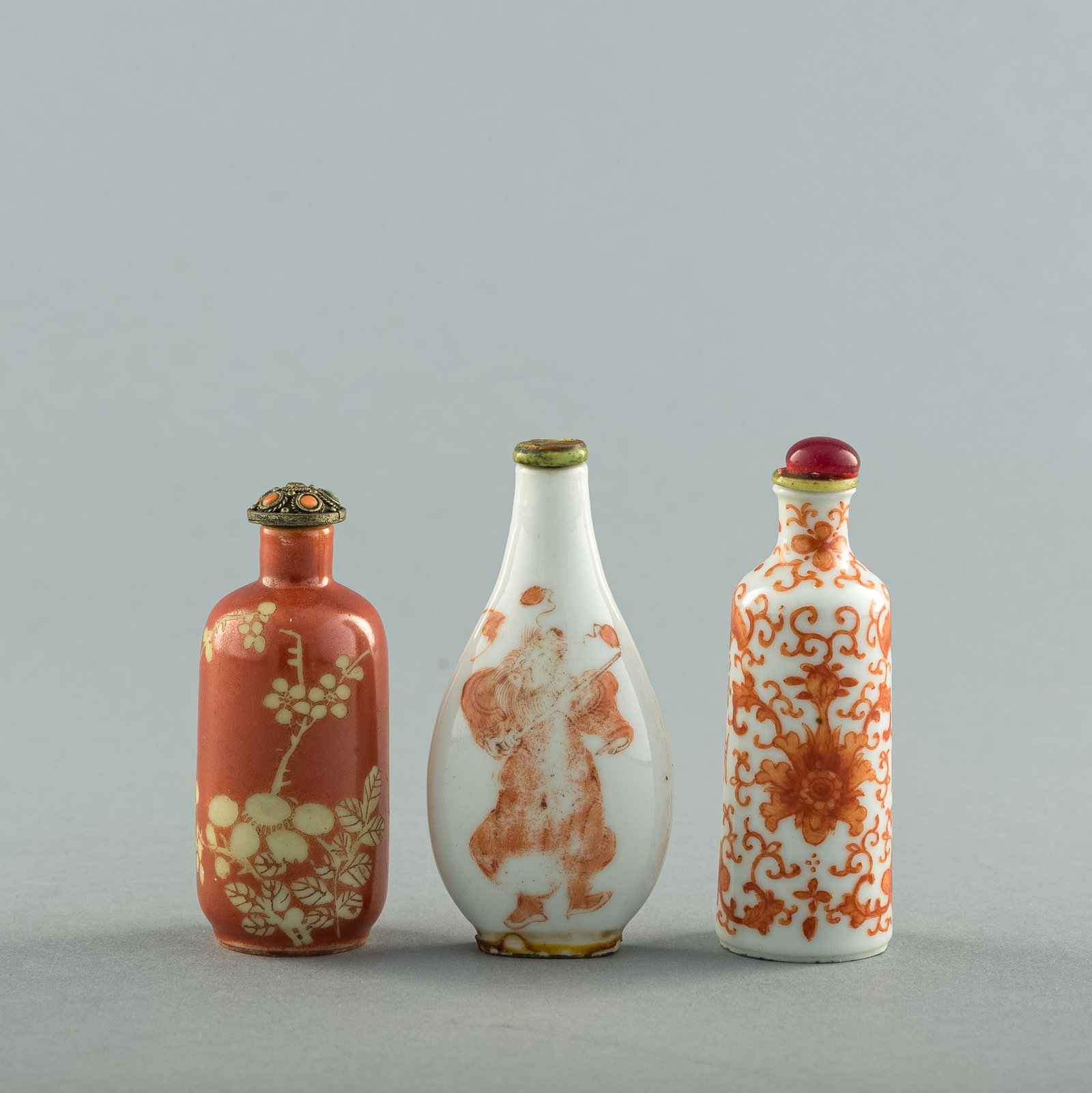 Three Chinese iron-red snuff bottles, 19th century: Three Chinese iron-red snuff bottles 19th century Comprising a scroll and bat-ground bottle with six-character mark; an iron-red-ground bottle with flowers; and a bottle with shou and figure with four