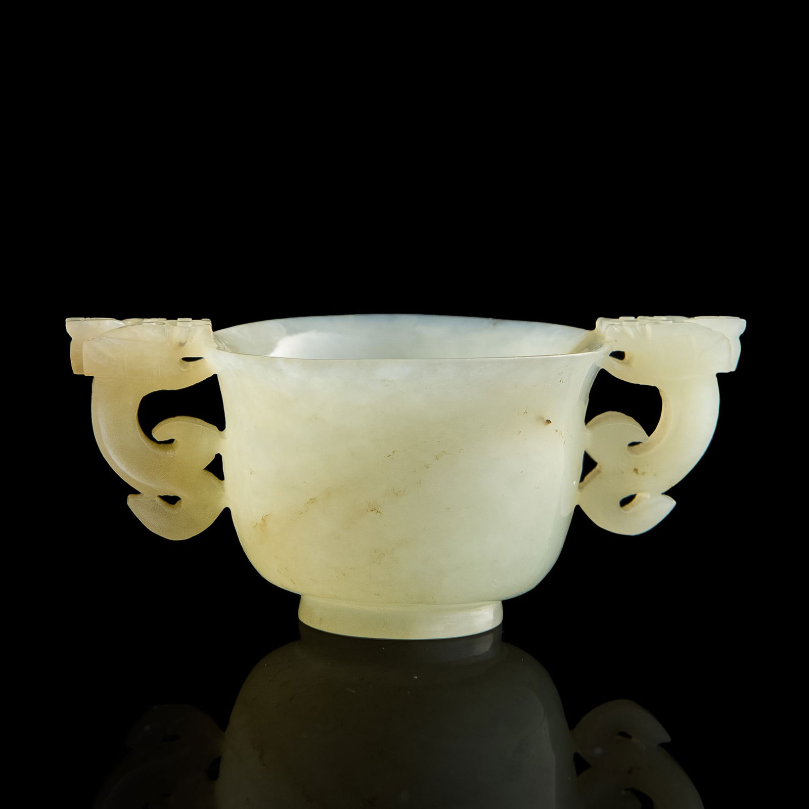 A Chinese carved white jade double-handled cup, Ming dynasty: A Chinese carved white jade double-handled cup Ming dynasty Each dragon head handle appears to bite the flared cup rim. H: 1 1/2, W: 3 1/4, D: 2 in. (H: 3.81, W: 8.26, D: 5.08 cm.) Provenance: Private