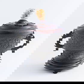 A Chinese bronze gui-form censer, Ming dynasty: A Chinese bronze gui-form censer Ming dynasty The lid set with a decorative jade, the body elaborately casted with auspicious motifs in relief. Sold with associated wooden stand. H: 8 1/8, W: 8 1/2, D