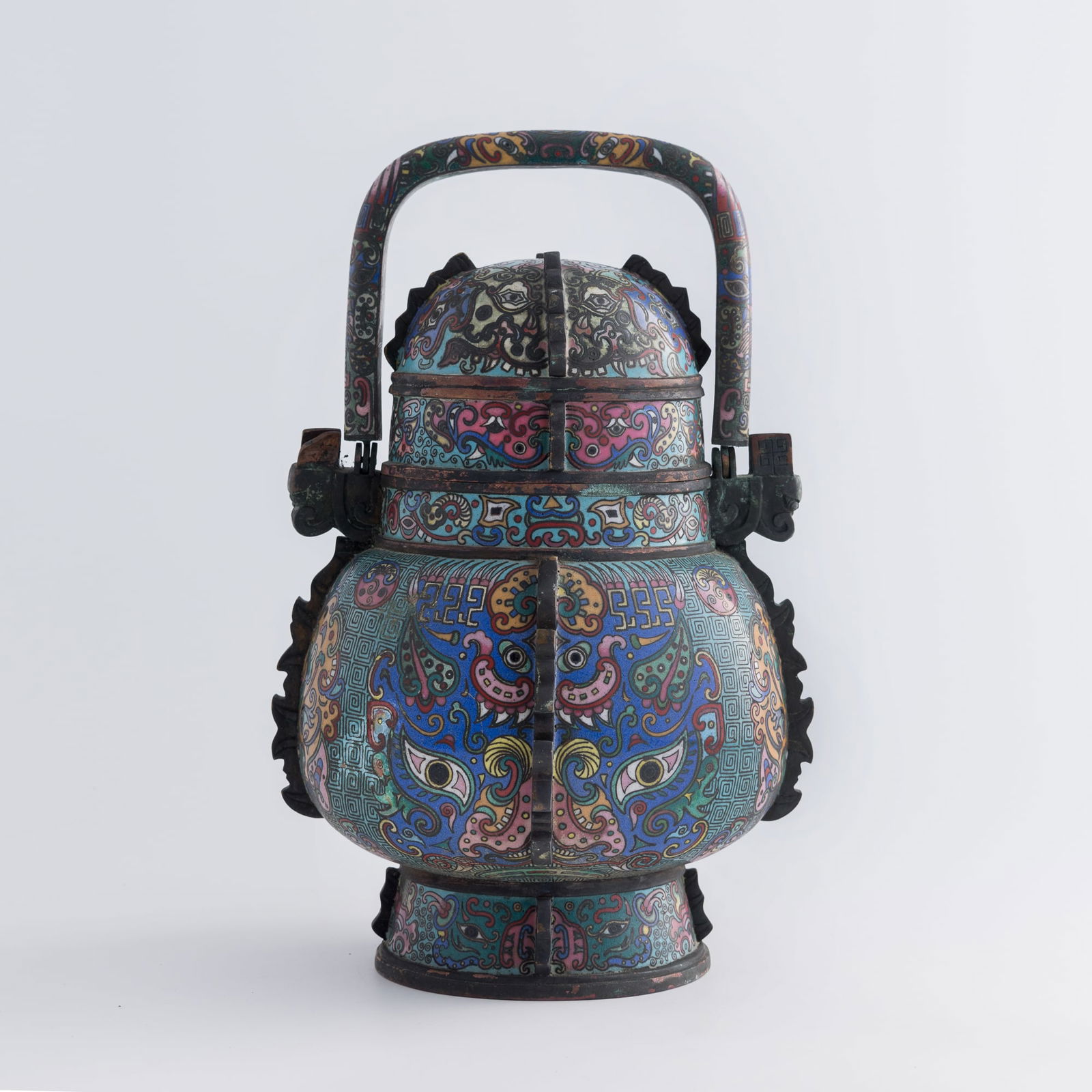 A Chinese cloisonne swing-handled you vessel, late 18th century: A Chinese cloisonne swing-handled you vessel late 18th century Decorated with key-fret patterns on a blue ground and various beast masks. H: 12 1/4, W: 8, D: 7 in. (H: 31.1, W: 20.3, D: 17.8 cm.) From