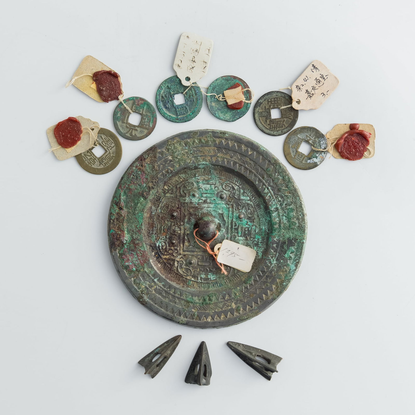 A Chinese bronze mirror, three arrowheads, and six coins, Han/Qing dynasty: A Chinese bronze mirror, three arrowheads, and six coinsHan/Qing dynastyDia: 4 1/4, D: 3/8 in. (Dia: 10.8, D: 1 cm. (mirror))Weight: 260.32 g (overall)From Dr. Lau, Honolulu, Hawaii. Acquired in Hong