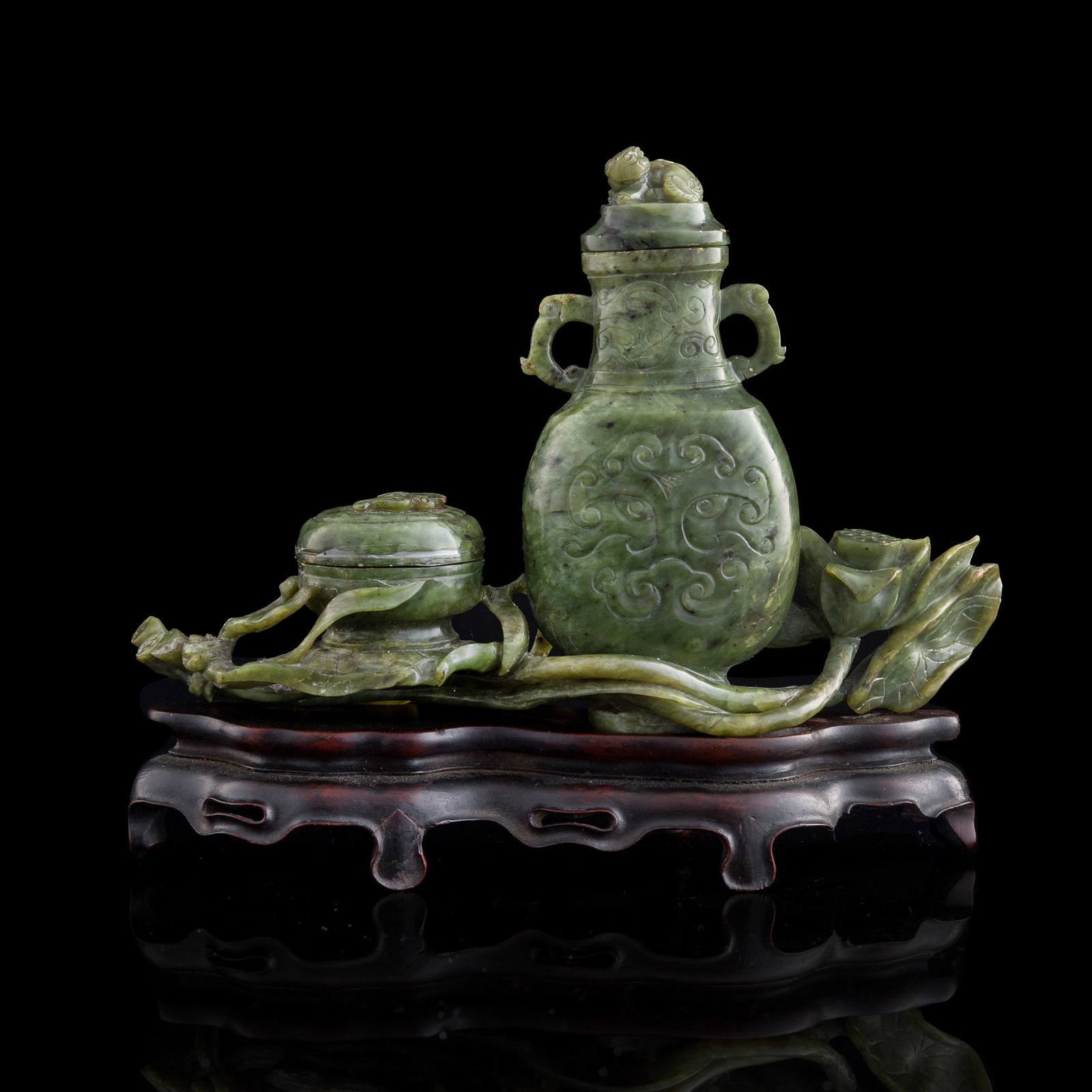 A Chinese carved spinach jade scholar's set, early 19th century: A Chinese carved spinach jade scholar's set early 19th century The set is carved with a box and a vase supported by lotus sprays. Sold with original hardwood stand. H: 6 1/2, W: 7 3/4, D: 1 1/2 in. (H