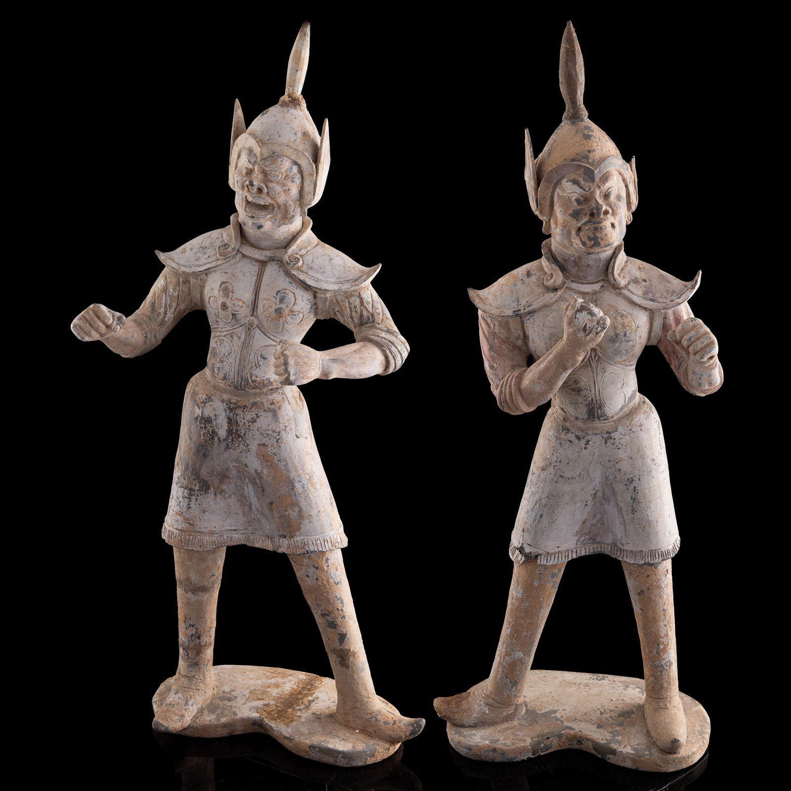 A pair of Chinese gray pottery warrior figures, Tang dynasty (618-907 AD): A pair of Chinese gray pottery warrior figures Tang dynasty (618-907 AD) Each figure is modeled standing with hands clasped before the chest, dressed in detailed armor and a crested helmet. Reportedly