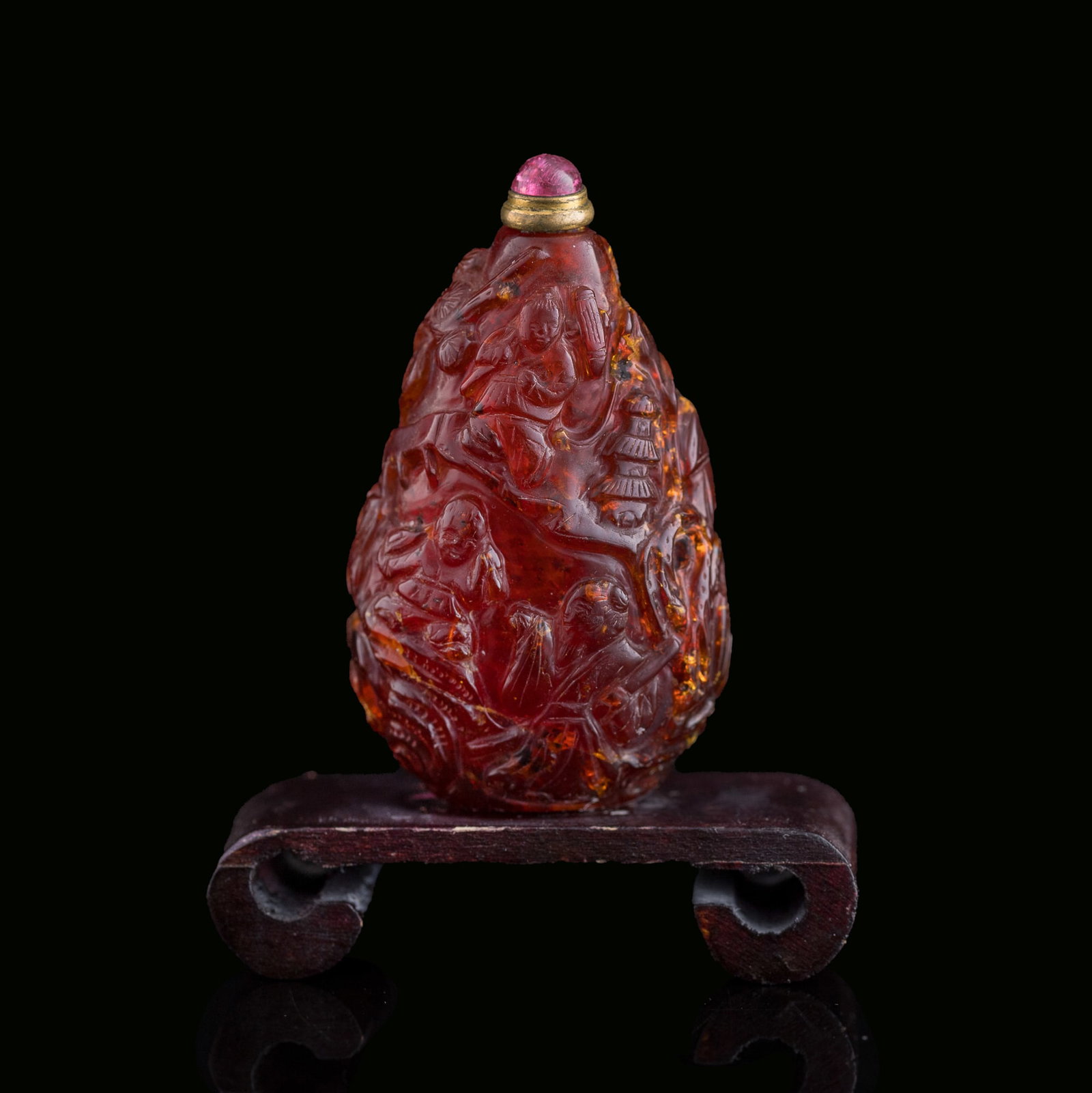A Chinese amber 'figural' and 'landscape' snuff bottle, 19th century: A Chinese amber 'figural' and 'landscape' snuff bottle 19th century Sold with associated wooden stand. H: 2 1/2, W: 1 3/8, D: 1 in. (H: 6.4, W: 3.5, D: 2.5 cm. (snuff bottle)) Weight: 19.3 g (amber) P