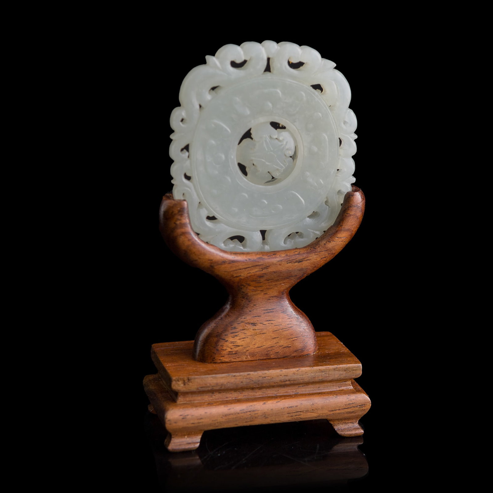 A Chinese carved white jade rotating-center pendant, 18th century: A Chinese carved white jade rotating-center pendant 18th century Sold with associated wooden stand. H: 2 1/8, W: 1 7/8, D: 3/16 in. (H: 5.4, W: 4.8, D: 0.5 cm. (jade)) From Mr. Tinero, Calabasas,