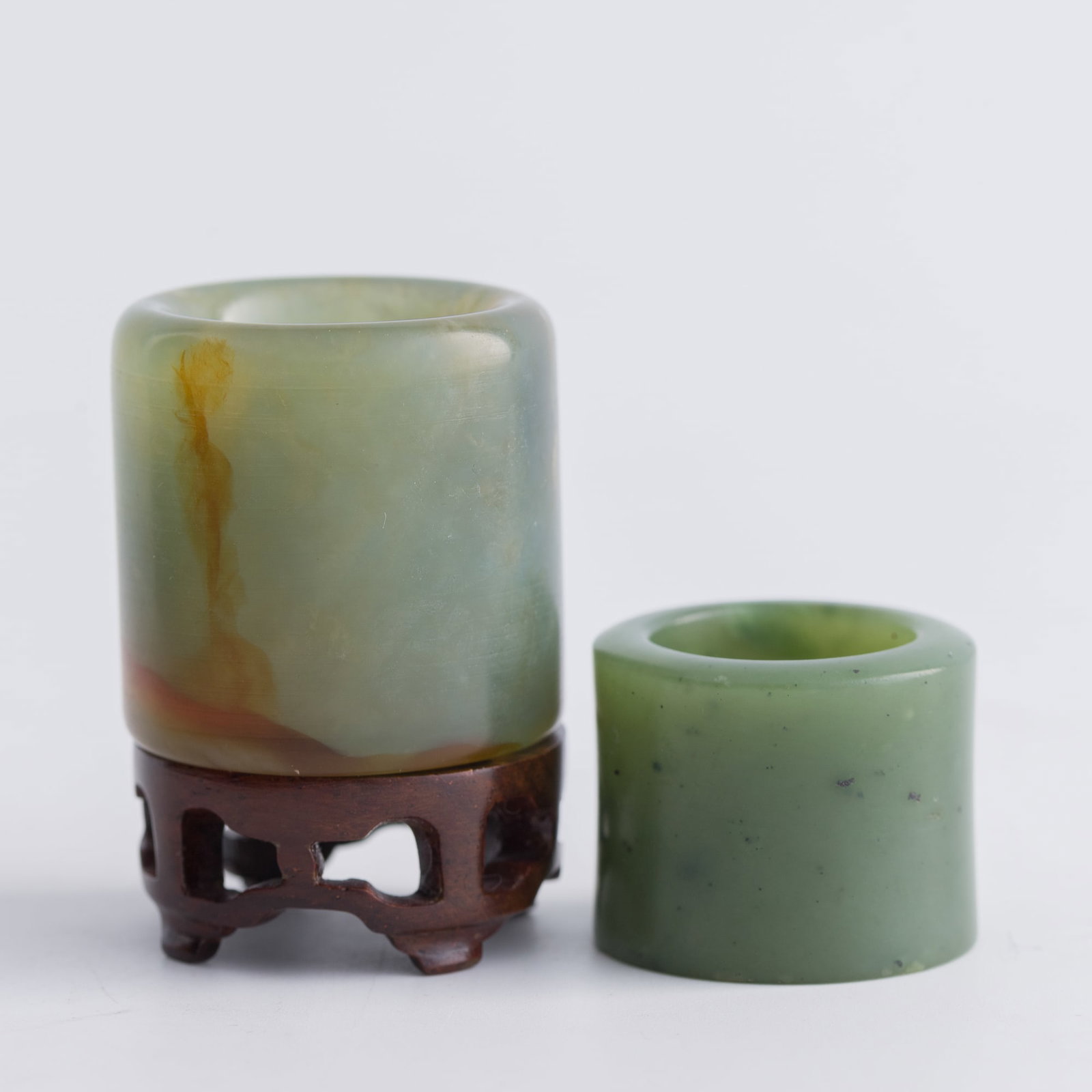 A Chinese jadeite and a spinach jade archer's ring, Qing dynasty: A Chinese jadeite and a spinach jade archer's ring Qing dynasty Sold with one associated wooden stand. (2). Inner Dia.: 22.5 mm, H: 34.8 mm (largest) From Mrs. Kiang in Newport Coast, California; coll