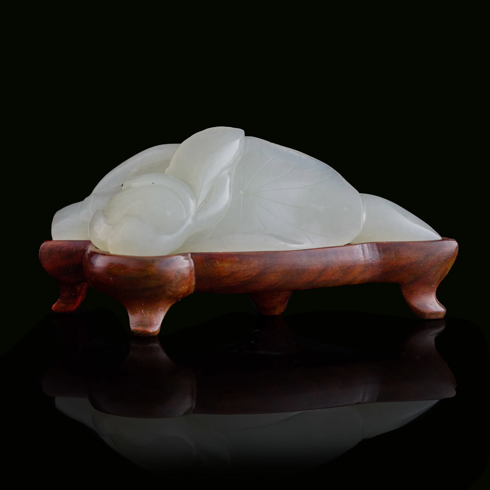A Chinese carved white jade 'lotus-leaf' pendant, 19th century: A Chinese carved white jade 'lotus-leaf' pendant 19th century Sold with associated wooden stand. H: 1 1/8, W: 3 1/4, D: 1 in. (H: 2.9, W: 8.3, D: 2.5 cm. (pendant)) From Mr. Chen, Great Neck, New York