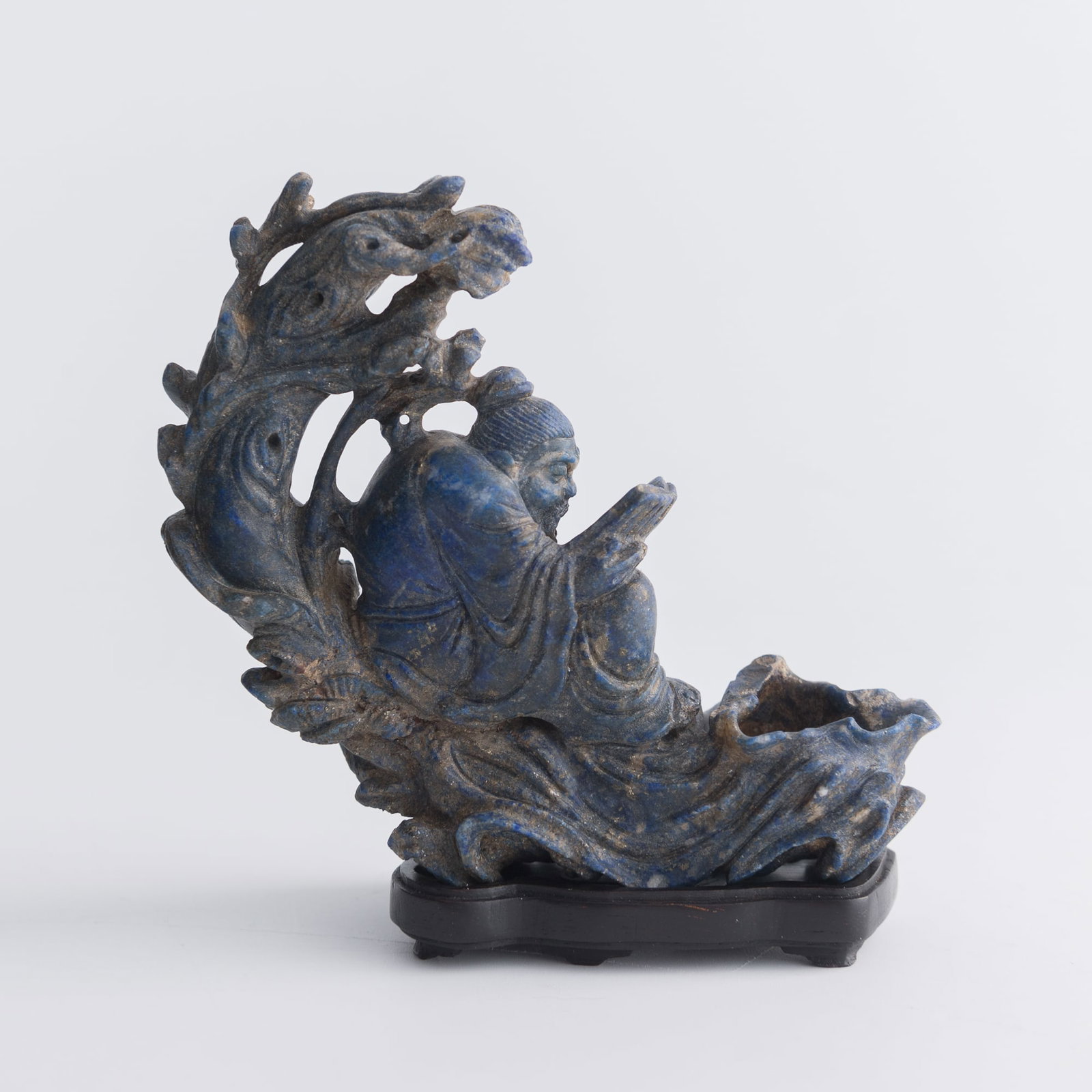 A Chinese lapis carving of an immortal riding a raft, late 18th century: A Chinese lapis carving of an immortal riding a raft late 18th century Sold with original hardwood stand. H: 3 3/8, W: 3 3/8, D: 1 1/4 in. (H: 8.6, W: 8.6, D: 3.2 cm. (overall)) Weight: 114 g (lapis) 