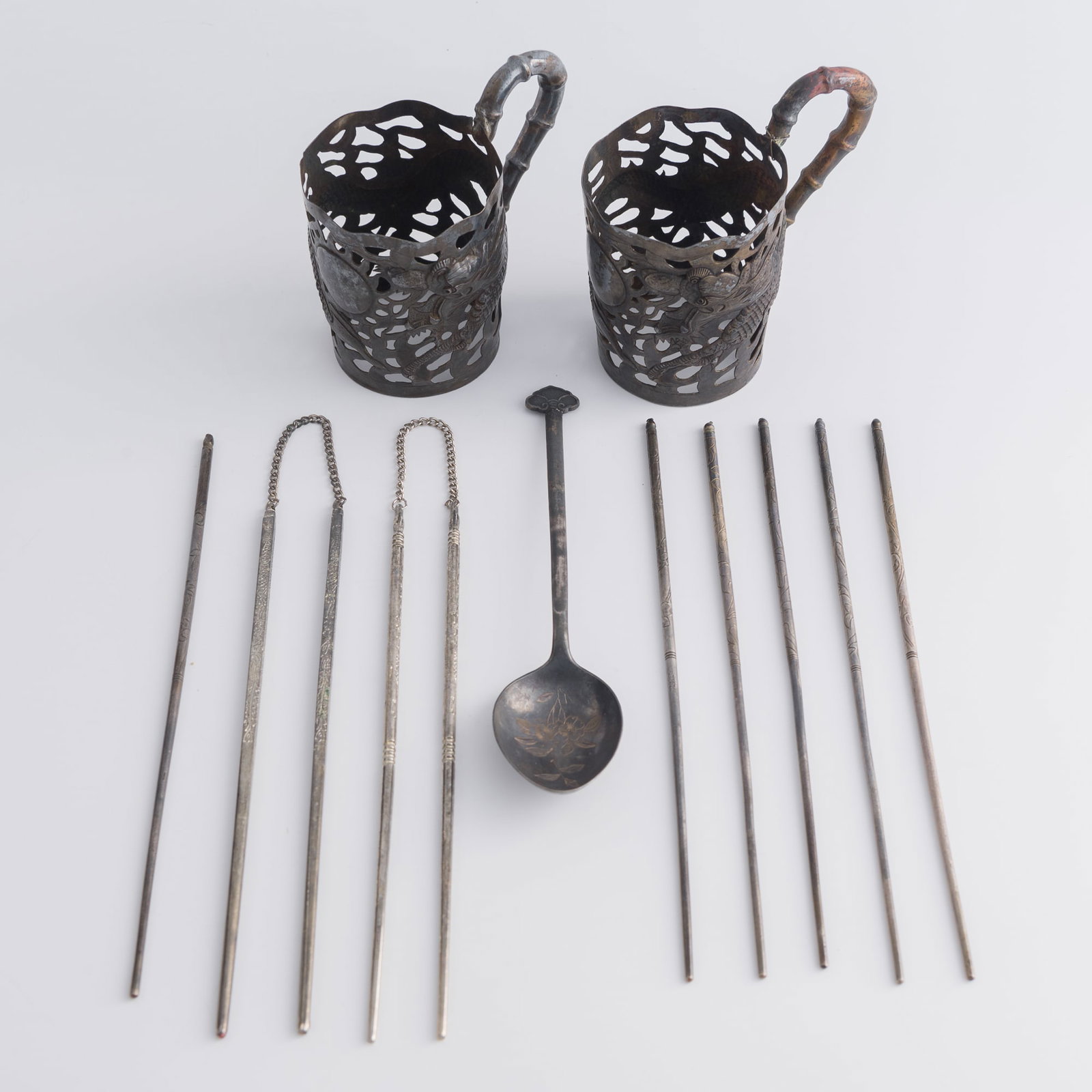 A group of Chinese silver ware, Qing dynasty/Republic period: A group of Chinese silver ware Qing dynasty/Republic period Comprising two cup sleeves, ten chopsticks, and a spoon. (13). H: 4, W: 4 1/4, D: 2 3/4 in. (H: 10.2, W: 10.8, D: 7 cm. (cup sleeve)) Weight