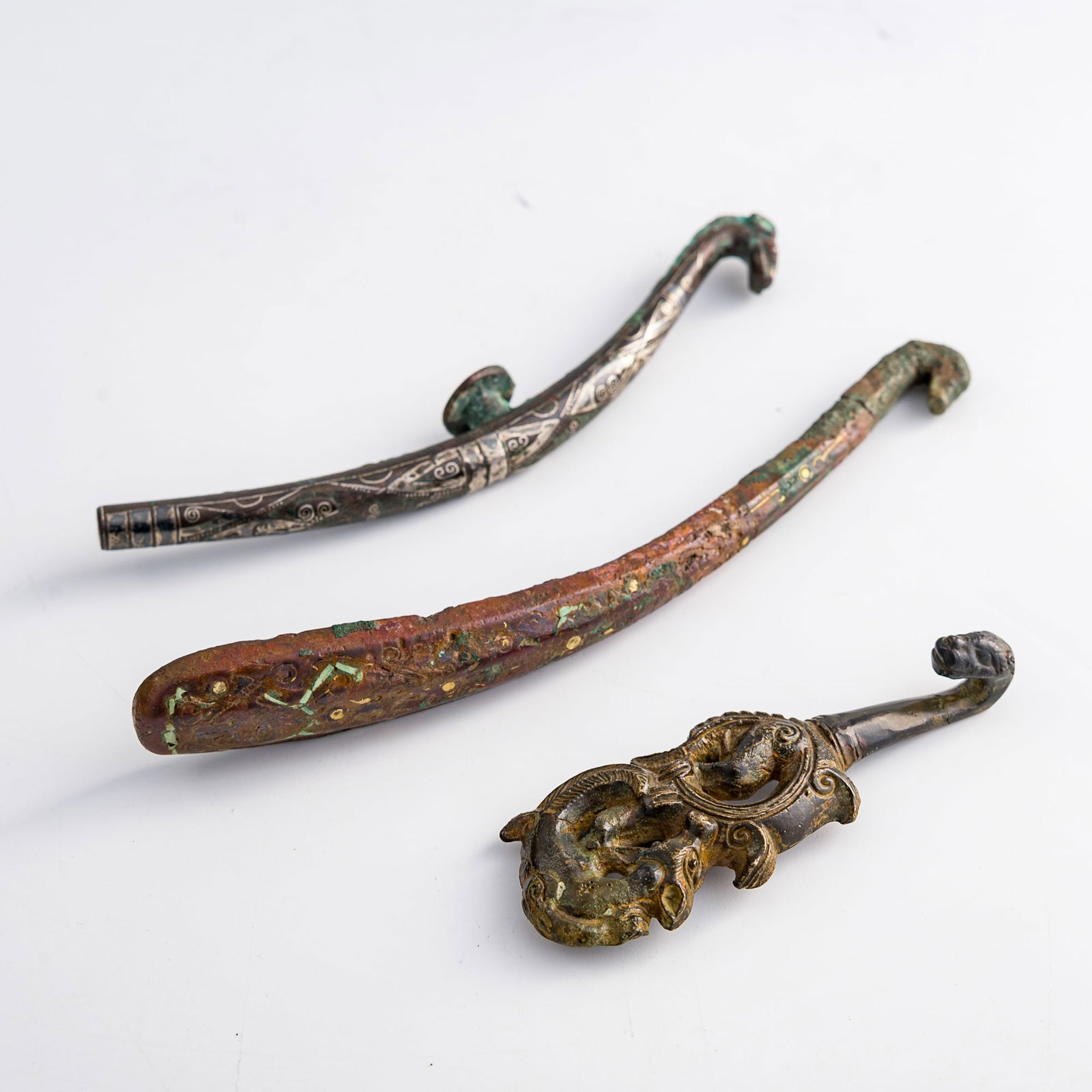 Three Chinese bronze belt hooks, Warring States period or later: Three Chinese bronze belt hooks Warring States period or later H: 1, W: 7 1/4, D: 1 1/4 in. (H: 2.5, W: 18.4, D: 3.2 cm. (largest)) Weight: 377.2 g (overall) Private collection, Charlottesville,