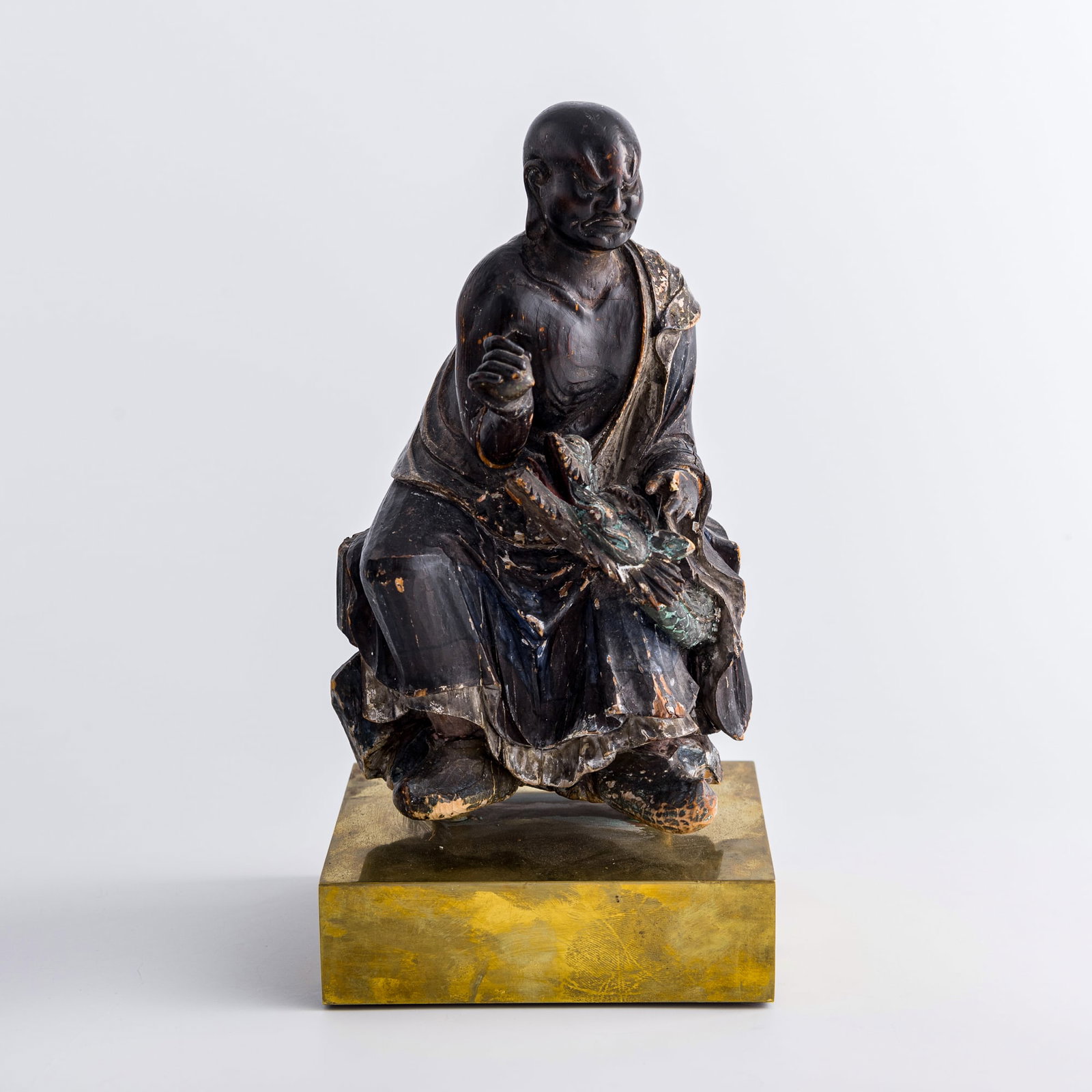 A Chinese wood carving of Xianglong Luohan, Ming dynasty: A Chinese wood carving of Xianglong Luohan Ming dynasty Sold with associated stand. H: 10 3/4, W: 5 1/2, D: 5 in. (H: 27.3, W: 14, D: 12.7 cm. (overall)) Private collection, Okemos, Michigan.