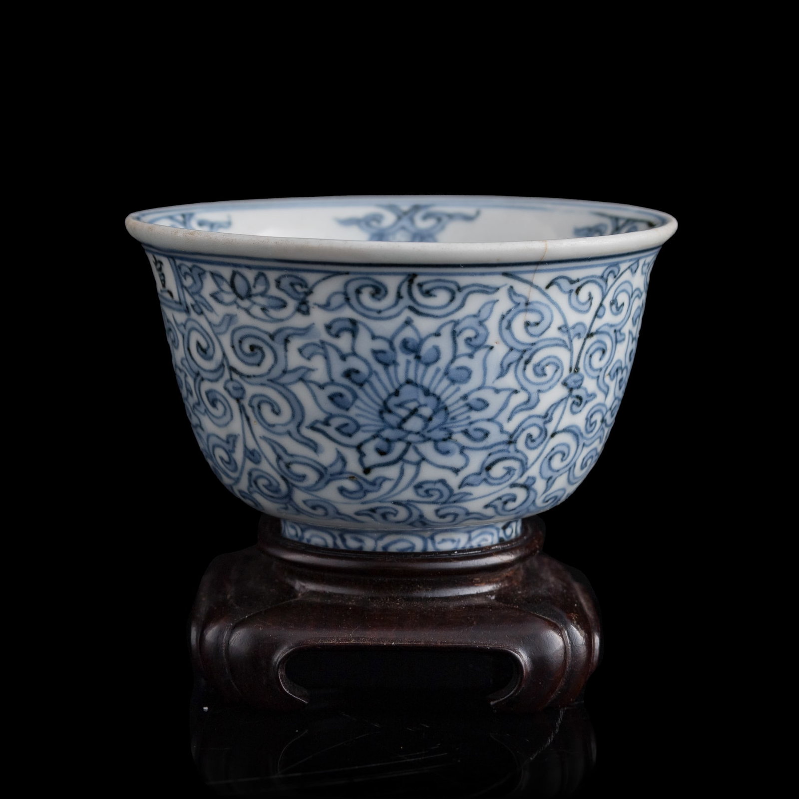 A Chinese blue and white 'lotus scroll' cup, late Ming dynasty: A Chinese blue and white 'lotus scroll' cup late Ming dynasty With four-character mark to body. Sold with associated hardwood stand. H: 2 1/8, Dia: 3 1/2 in. (H: 5.4, Dia: 8.9 cm. (cup)) From Mr. Kwok