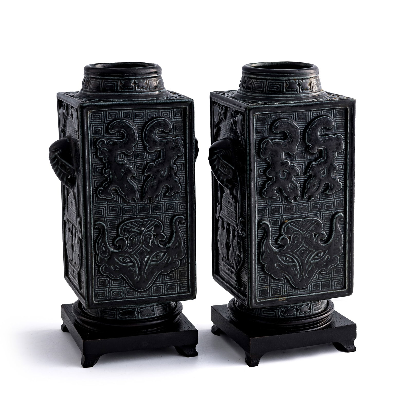 A pair of Chinese archaistic bronze-glazed 'taotie' cong-form vases, Republic period: A pair of Chinese archaistic bronze-glazed 'taotie' cong-form vases Republic period Each with six-character mark to underside. Sold with two associated wooden stands. (2). H: 7 5/8, W: 4 3/4, D: 3 3/8