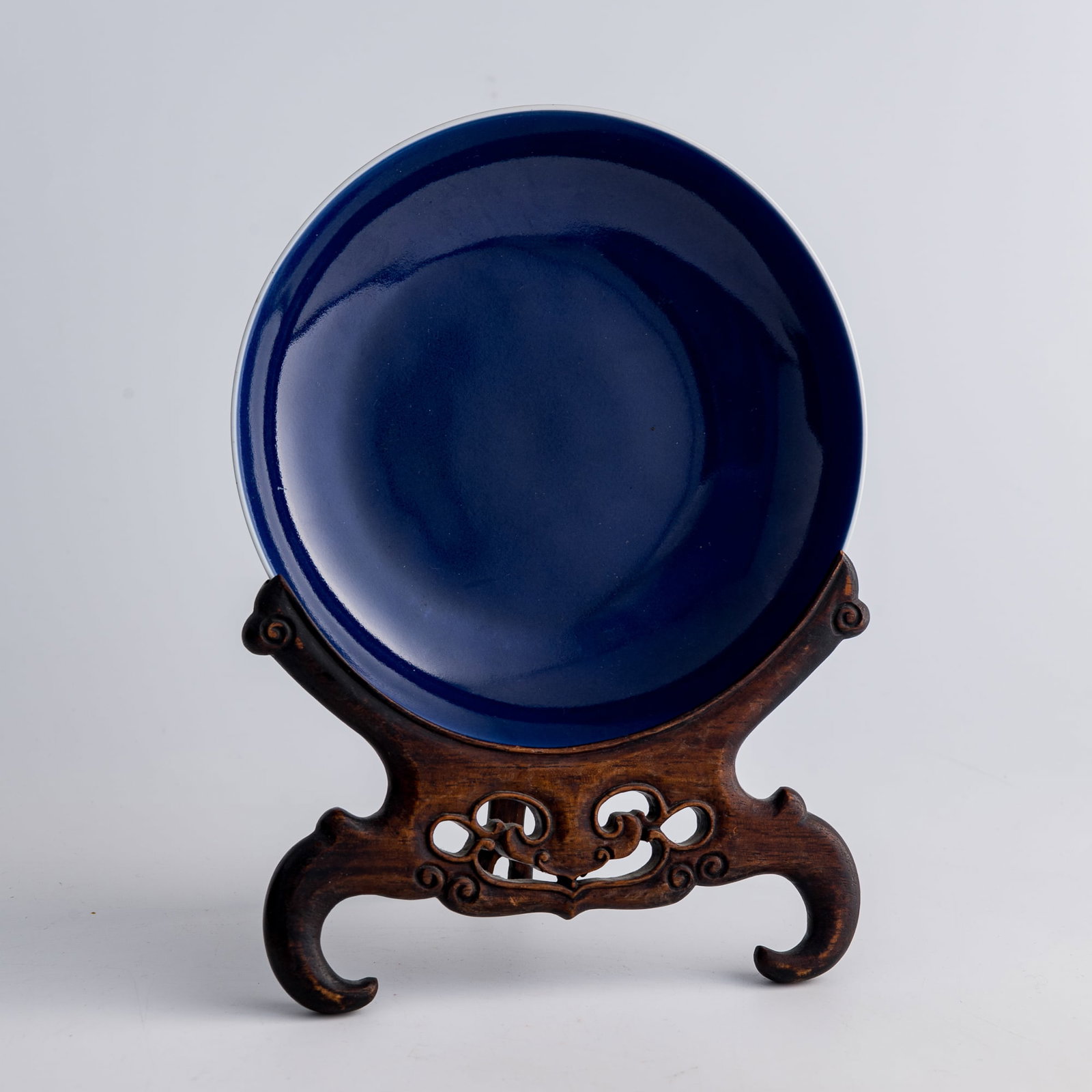 A Chinese sacrificial-blue glazed dish, Qianlong period, Qing dynasty: A Chinese sacrificial-blue glazed dish Qianlong period, Qing dynasty With six-character Qianlong mark and old stickers to underside. Sold with associated wooden stand. H: 1 1/2, Dia: 6 1/2 in. (H: 3.8