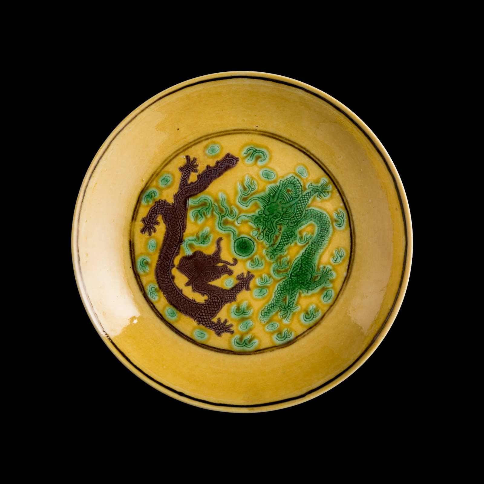 A Chinese yellow-ground sancai 'dragon' dish, Guangxu period, Qing dynasty: A Chinese yellow-ground sancai 'dragon' dish Guangxu period, Qing dynasty Depicting two dragons chasing a flaming pearl, rendered in green and purple enamels against a yellow ground. The exterior is p