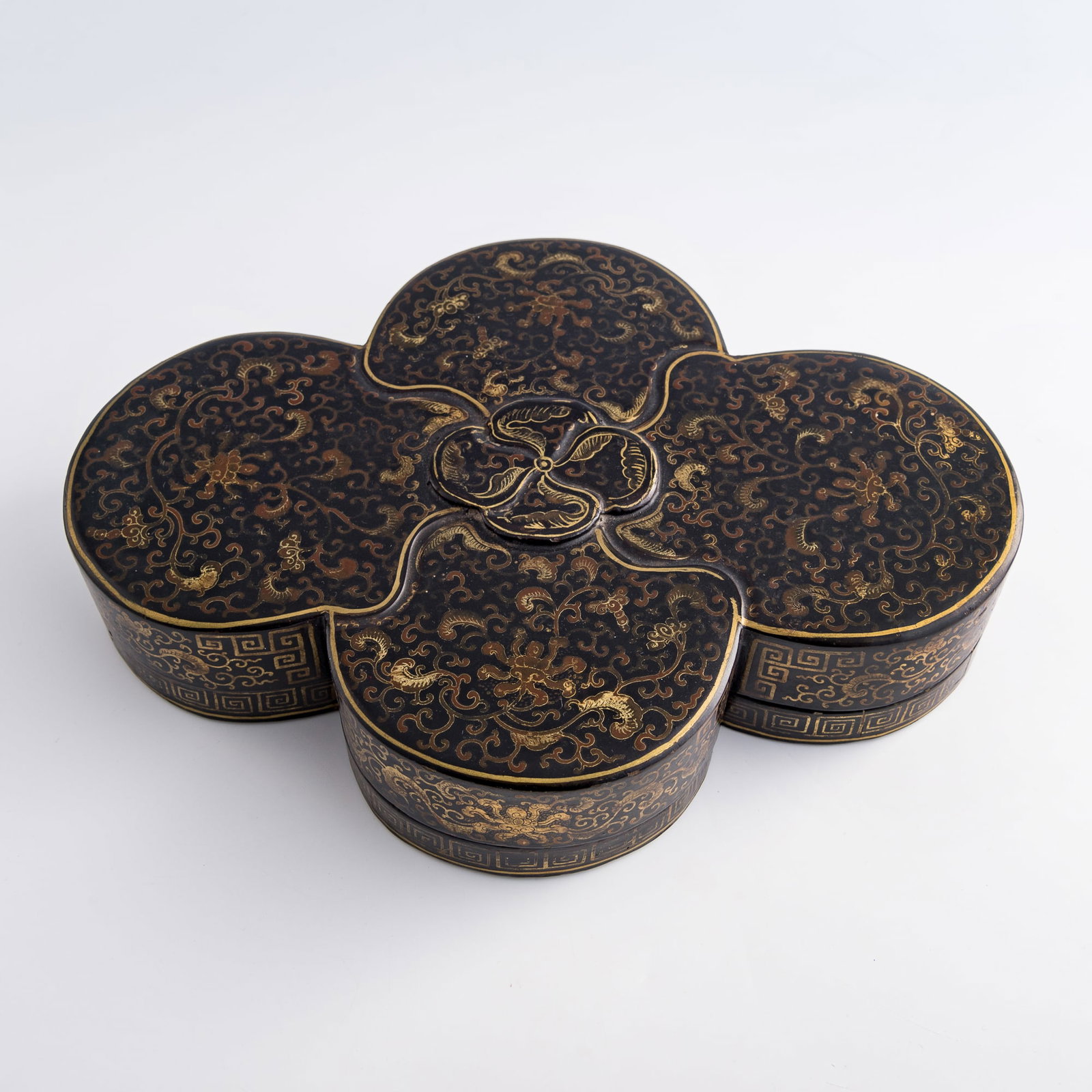 A Chinese gilt-lacquer quatrefoil lidded box, Qianlong period, Qing dynasty: A Chinese gilt-lacquer quatrefoil lidded box Qianlong period, Qing dynasty Accented in gilt and red and decorated throughout with floral scrolls and 'hui' motifs. H: 2 7/8, W: 14, D: 10 1/2 in. (H: 7.