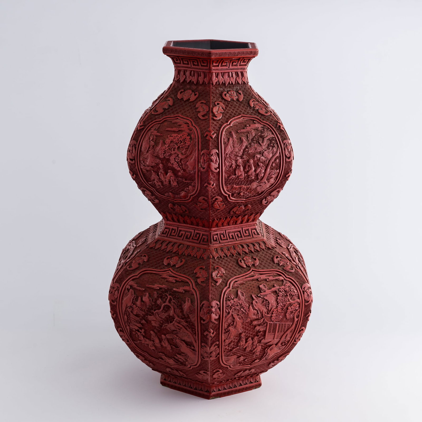A Chinese hexagonal cinnabar double-gourd vase, Qianlong period, Qing dynasty: A Chinese hexagonal cinnabar double-gourd vase Qianlong period, Qing dynasty Of hexagonal double-gourd form, the vase is deeply carved with shaped panels depicting figures in pavilion landscapes. The 