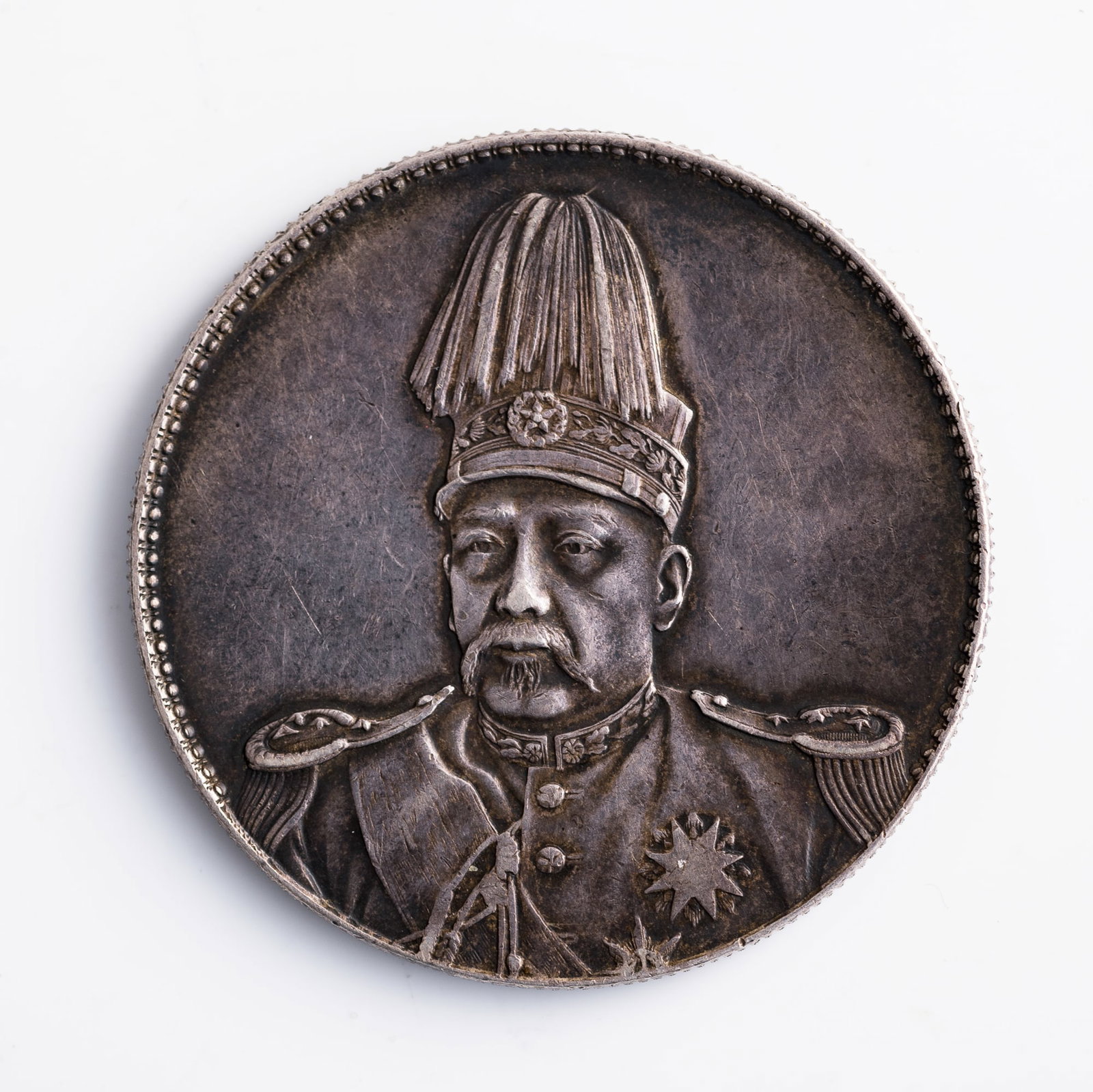 A Chinese Yuan Shikai 'plumed hat' commemorative silver dollar, 1914: A Chinese Yuan Shikai 'plumed hat' commemorative silver dollar 1914 Dia: 38.8, D: 2.5 mm. Weight: 27 g From a private collector in San Jose, California; inherited from his father in Shanghai.