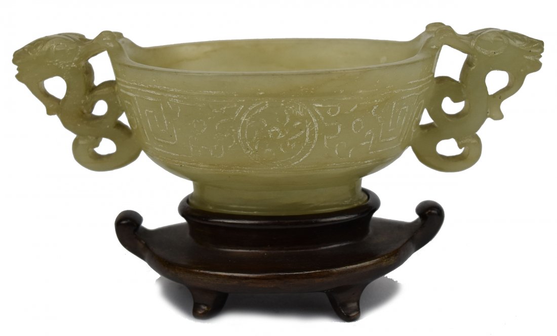 White Jade Cup with Chilong Handles, Ming Dynasty: A Chinese White Jade Cup with Chilong Handles, Ming Dynasty (1368-1644) This cup, carved from white jade is adorned with two exterior chilongs and sits upon a wood base. The chilongs have their claws