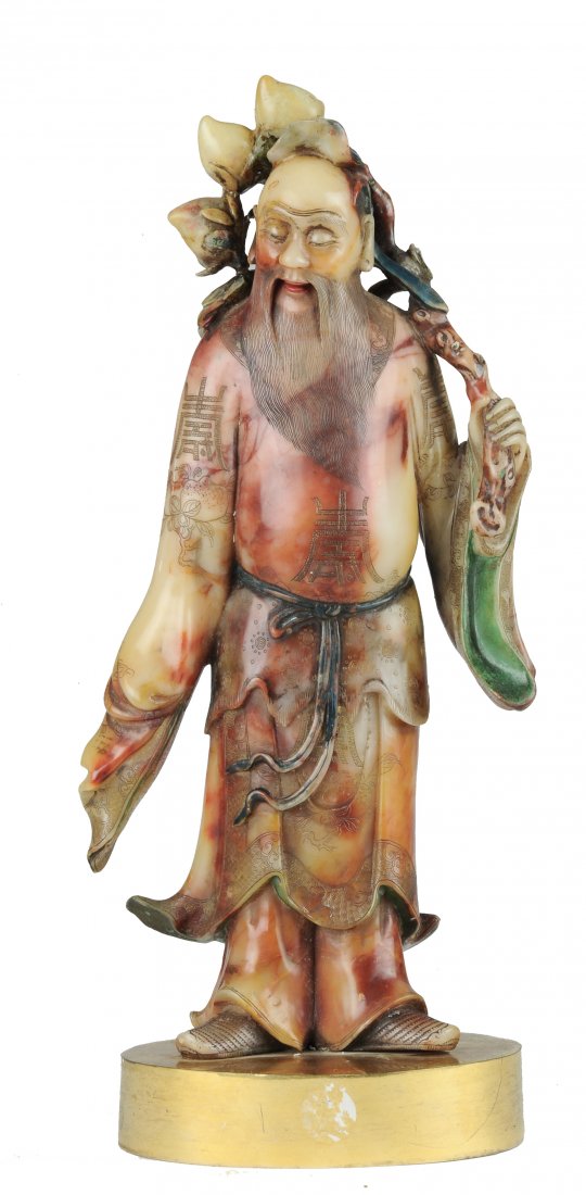 A Soapstone Carving of Dong Fang Suo: Colorfully painted soapstone carving of Dong Fang Suo holding a branch of three peaches from the 18th - 19th century. Dong Fang Suo has a long beard and a downcast gaze. His robe is intricately carved