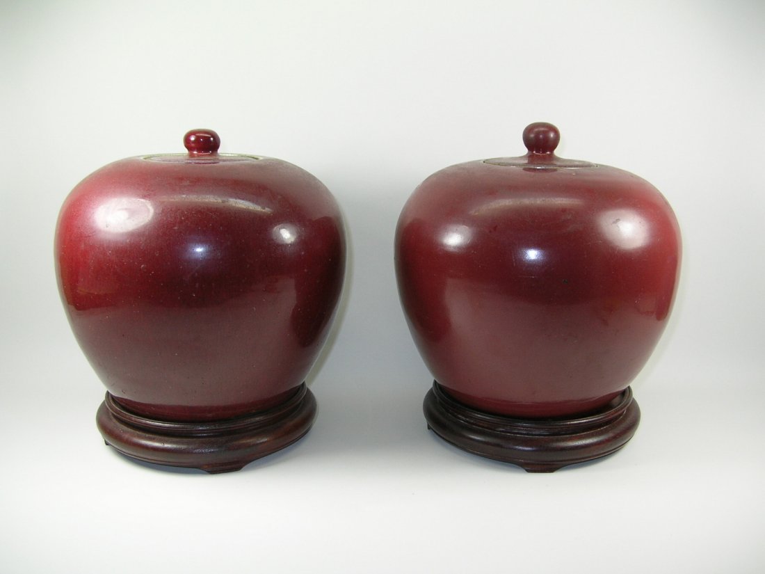 Pair of Chinese Ox-Blood Glaze Globular Jars 19th C: A pair of Chinese ox-blood / sang de boeuf glaze globular jars with covers and hardwood bases, one in good condition with only minor losses to inner rim of the mount (not seen if covered), the other r