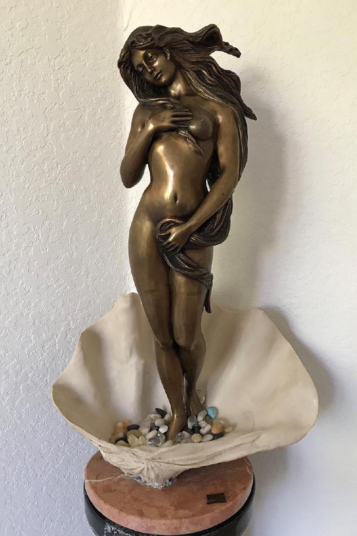 Manuel Vidal, Ebano made in Spain, Bronze nude female: Manuel Vidal, Ebano made in Spain, Bronze nude female standing in shell with polished tumbled loose rocks 34in. Tall x 21 in. wide on rose marble round base