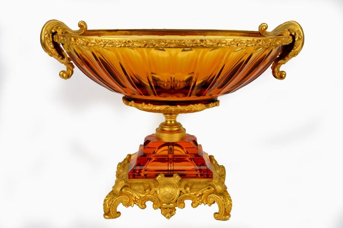 GILT BRONZE & AMBER GLASS CENTERBOWL. The bronze base: GILT BRONZE & AMBER GLASS CENTERBOWL. The bronze base centered by a shield crest holding an amber glass step to a gilt bronze stem, supporting an amber glass bowl with gilt bronze rim and gilt bronze 