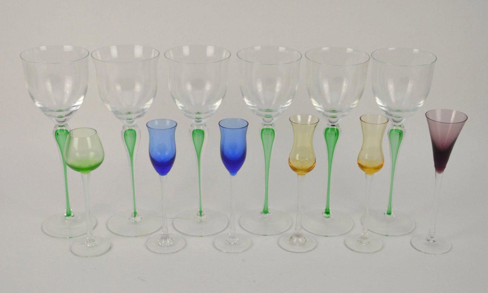 12 Pcs Clear and Colored Glass Stemware - Includes six: 12 Pcs Clear and Colored Glass Stemware - Includes six green stem wine glasses 10 1/8" H, two yellow cordial 7 3/4" h, two blue 7 1/2" H, one purple 8", one green 7" H. Condition: No damage identified