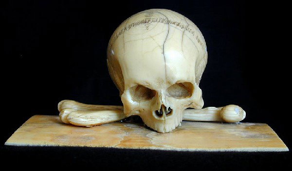 ANTIQUE IVORY SKULL & BONES CARVING DATED 1886 An : ANTIQUE IVORY SKULL & BONES CARVING DATED 1886 An intricately sculpted ivory human skull & bones carving on ivory plank base, signed Interlaken 1886, 4"L x 2"H, missing one bone.NOTE: Interlaken is Sw