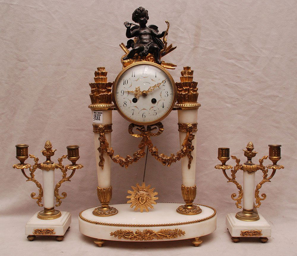 French gilt bronze and white marble 3 piece clock: French gilt bronze and white marble 3 piece clock garniture set, patinated bronze cupid at top of porcelain face, garland and bow, torch motif on oval base, double branch candelabra, (9"h x 6"w)