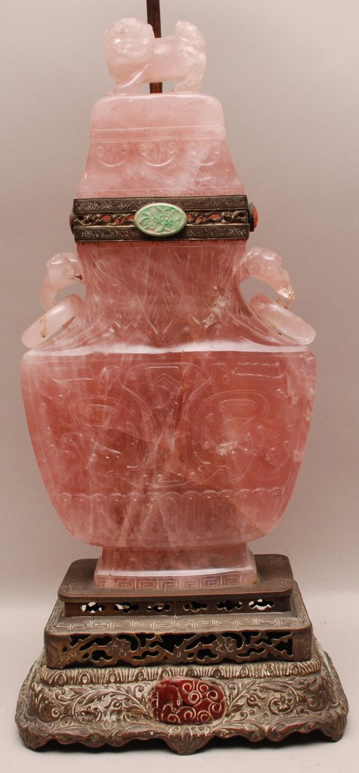 Large Rose Quartz Urn Bronze Mounted Lamp. The bronze : Large Rose Quartz Urn Bronze Mounted Lamp. The bronze base and connector have carved jade and agate mounts along with a jade finial. Condition: slight loss to the foo dog top. Otherwise normal wear. H