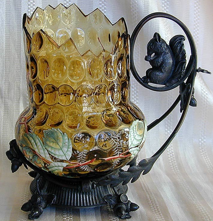 Victorian Enameled Thumbprint Pitcher w/ Squirrel: Victorian Enameled Thumbprint Pitcher w/ Squirrel Mounts Amber color glass in the form of a large nut container with an originally designed jagged and gilt top edge; amusing mounted to a silverplate s