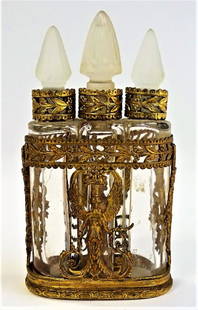 ANTIQUE FRENCH THREE BOTTLE PERFUME CLUSTER: Antique French triple bottle perfume cluster, held in openwork brass frame. Decorated with winged woman depictions and arrow in quiver side panels. Contains two half circle shaped bottles and one