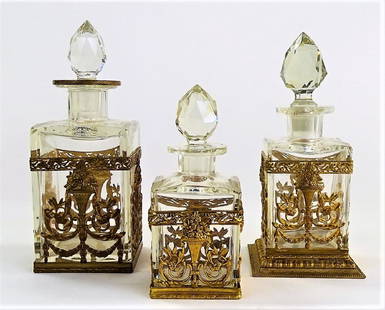 THREE VTG FRENCH BRASS MOUNTED SCENT BOTTLES: Collection of vintage French crystal scent bottles, in square form and graduated sizes, each with a facet cut stopper. All are mounted in ornate brass frames with floral bouquet sconces and floral