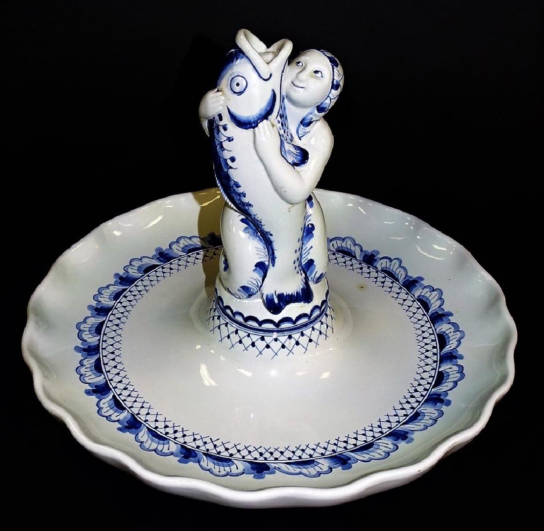 ROYAL COPENHAGEN ALUMINIA FAIENCE CENTERBOWL: Royal Copenhagen Aluminia Faience porcelain centerbowl, done in blue and white. Having a column in the figural form of a nude woman clutching a fish, decorated with a continous lattice and rocaille ba