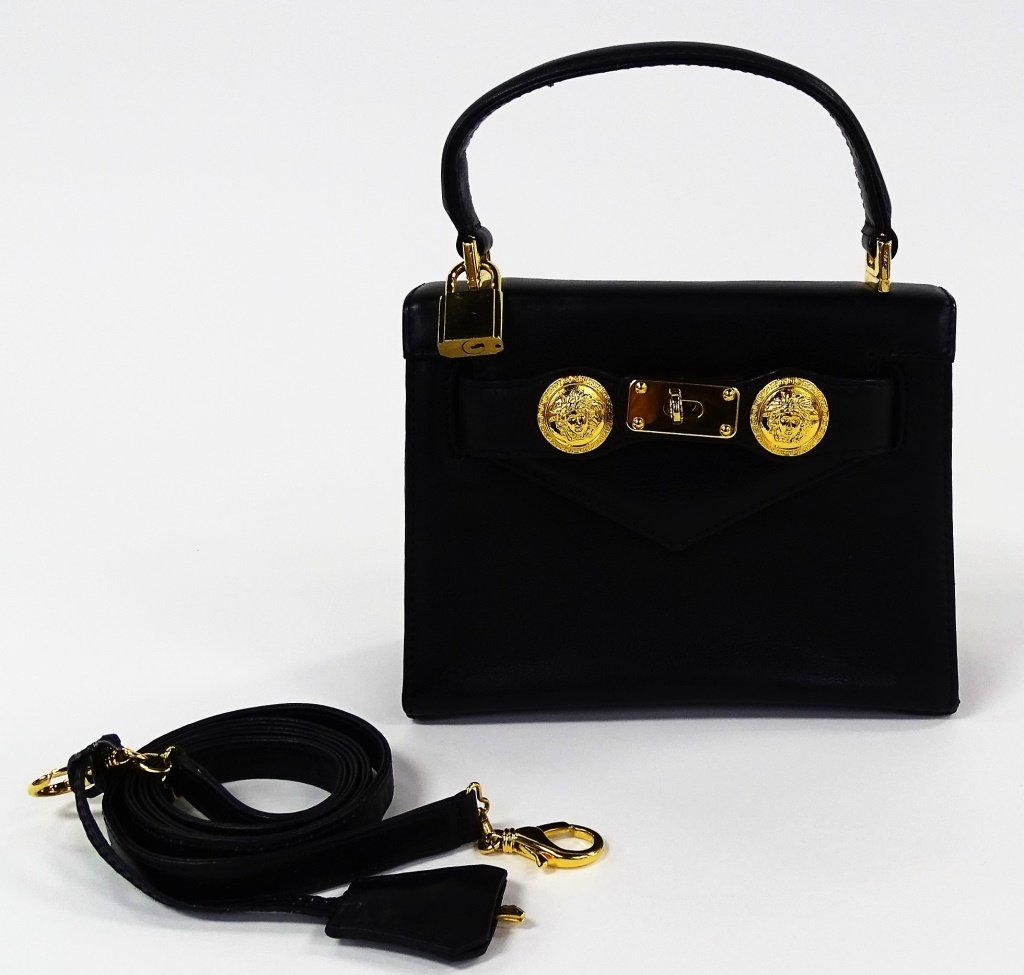 GIANNI VERSACE BLACK LEATHER MEDUSA CLUTCH HANDBAG: Gianni Versace black leather 'Medusa' evening clutch hand bag with strap, gold tone accents & lock. Locking mechanism featuring two buckles with Medusa head adornments, keys included. Opens to black l