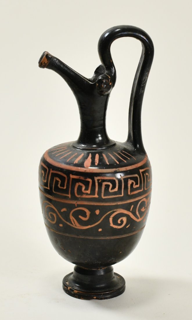 An Apulian Pottery Oinochoe: Height: 6 3/4 inches (17.1 cm.) 450-430 B.C. Ex- Edgar Owen, 1992. Decorated in two registers. Upper register is Greek key pattern. Lower register is scroll pattern. Raised on shoulder, two female hea