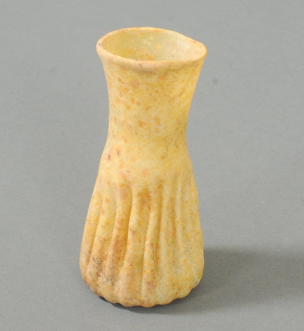 ANCIENT ROMAN VERTICAL RIBBED GLASS FLASK: Features vertical ribs on the body. Indented bottom which flares inwards. The weathering is of a cream color type. Circa 1st-2nd CenturyMeasurements: 2 3/5 in. H. (6.6 cm.)Ex: Prominent European colle