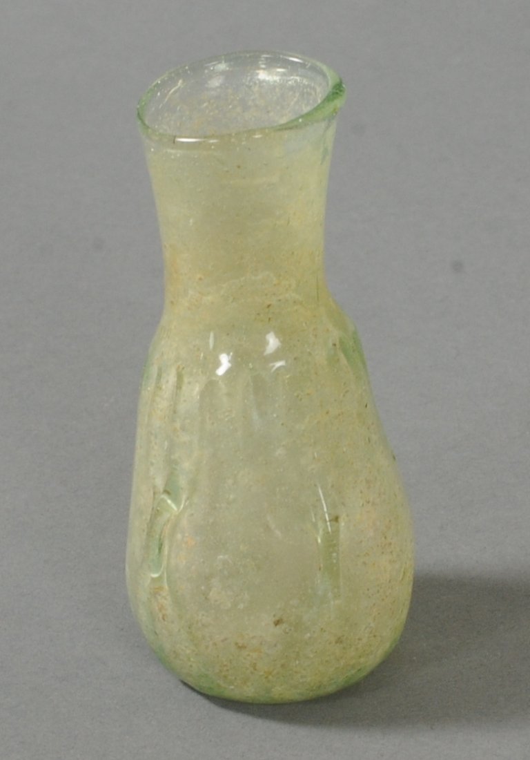 ANCIENT ROMAN GLASS FLASK: Beautiful shade of green. Vertical ribs on the body. The bottom is indented inwards. Soil deposits evident on the inside. Circa 1st-2nd Century A.D.Measurements: 2 4/5 in. H. (7.1 cm.)Ex: Prominent Eu