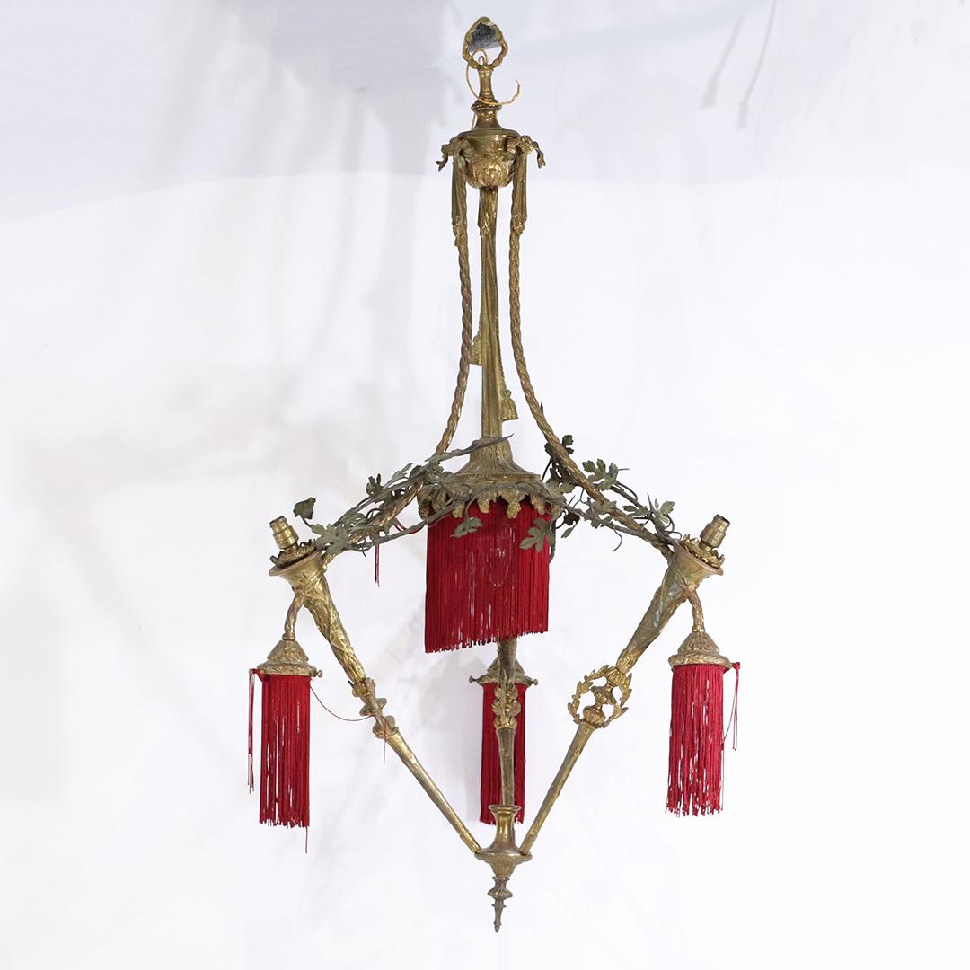 Antique French Empire Tripod Torches Brass Chandelier: Antique French Tripod Torches Brass Chandelier, has fitters for glass shades for top and bottom [not included]. Red fabric fringe accents, original brass patina finish. size: 37h x 19w